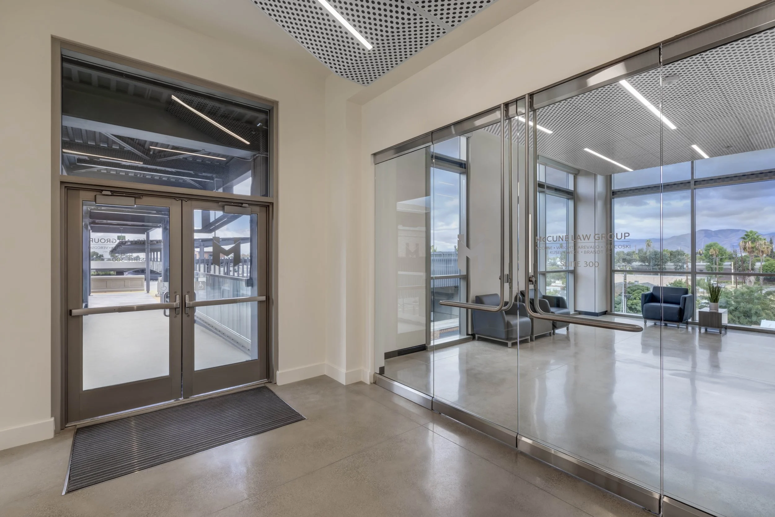 Modern office lobby with glass doors, chairs, and large windows showing a scenic view of mountains and trees.