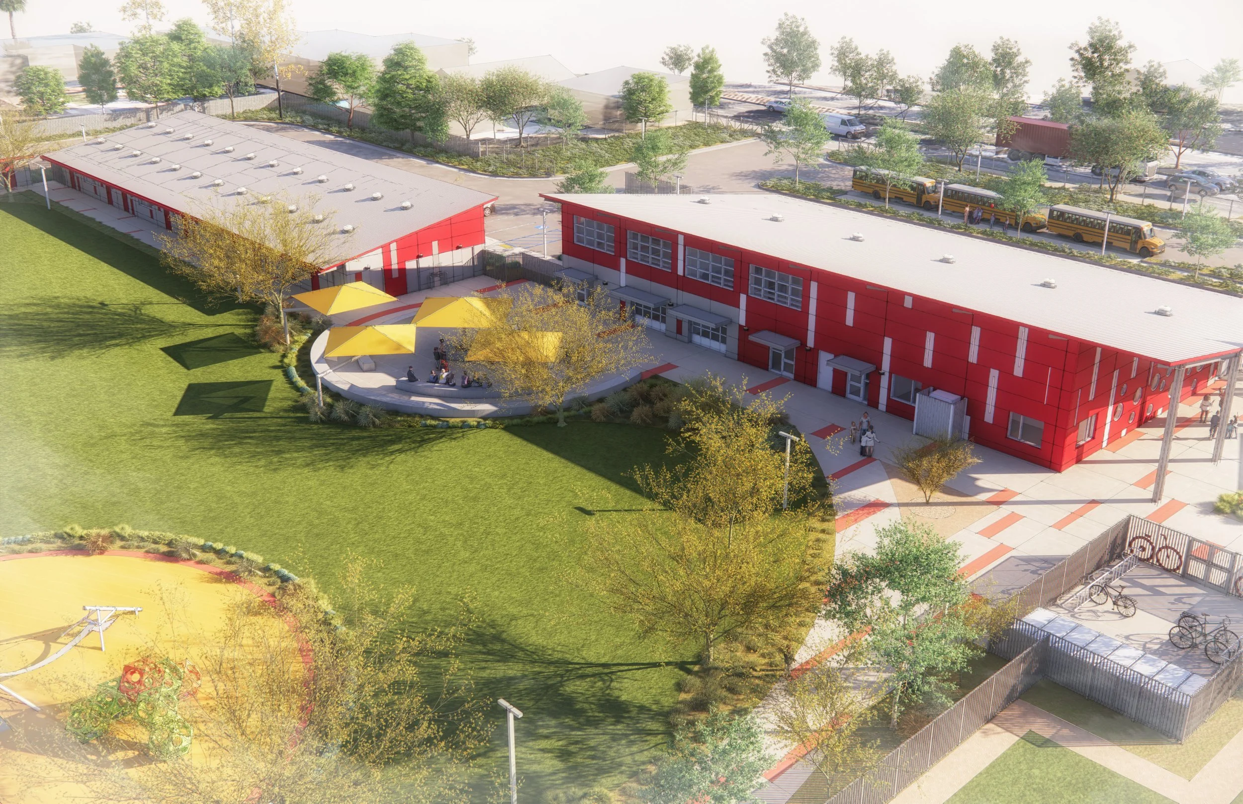 An aerial view of a modern school campus with red buildings, outdoor seating with yellow umbrellas, playground equipment, bicycles, trees, and a parking lot with yellow school buses.