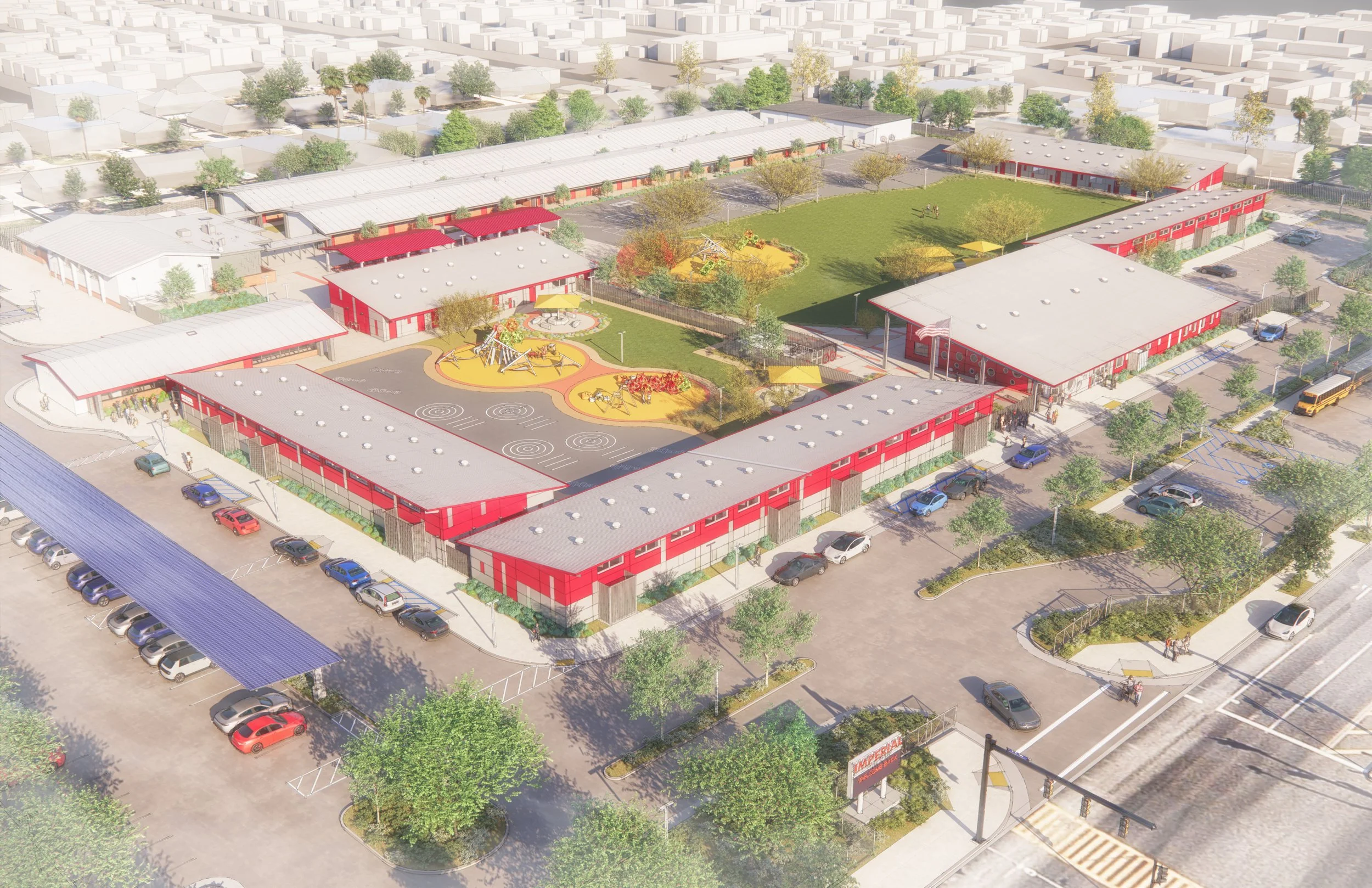 Aerial view of a school complex with multiple red and white buildings, a playground, a grassy field, trees, parking lot, and a bus on the street.