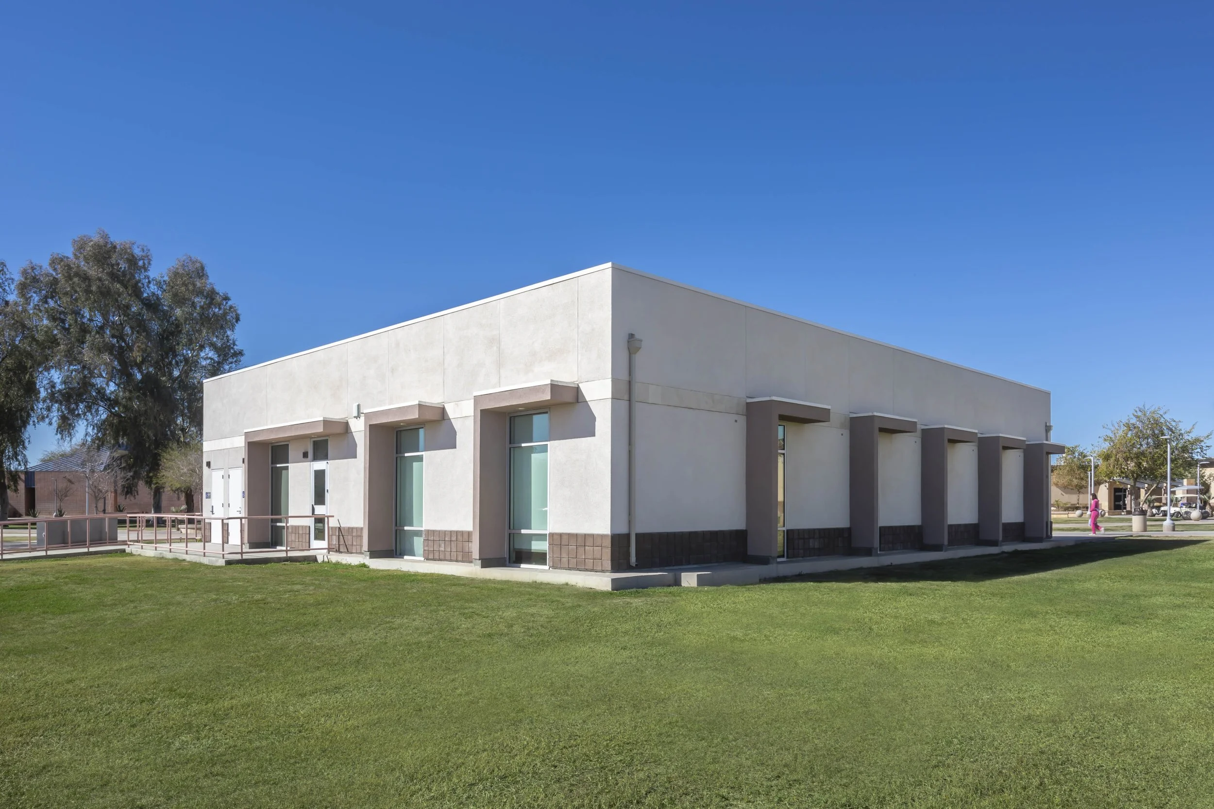 A modern, white, single-story building with large windows and a flat roof, surrounded by a grassy lawn under a clear blue sky.