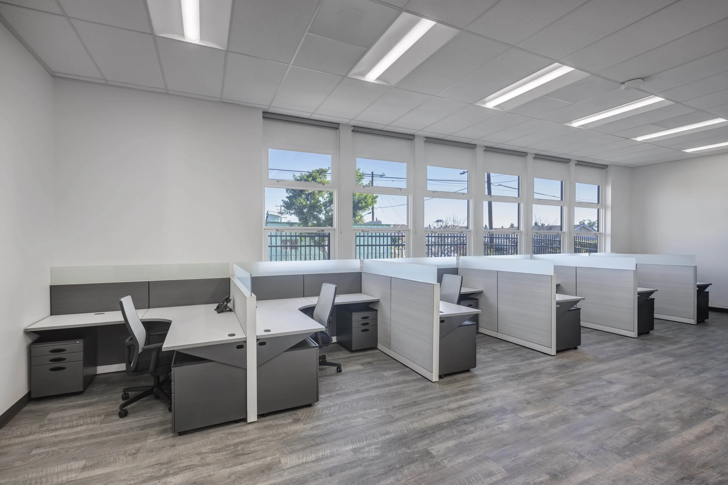 Empty modern office with cubicles, office chairs, and large windows with blinds