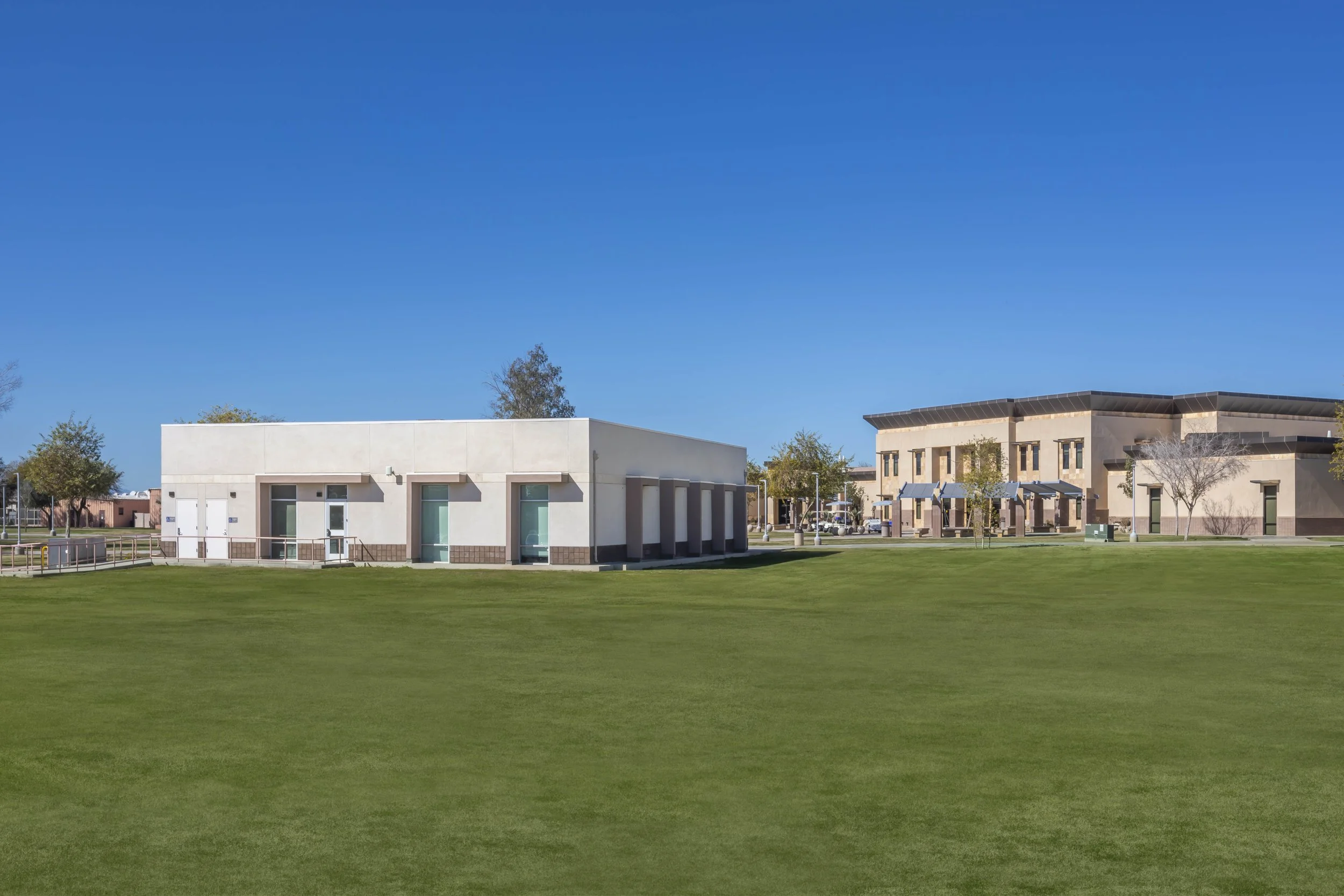 Wide view of a park with two modern buildings, lush green grass, and a clear blue sky.