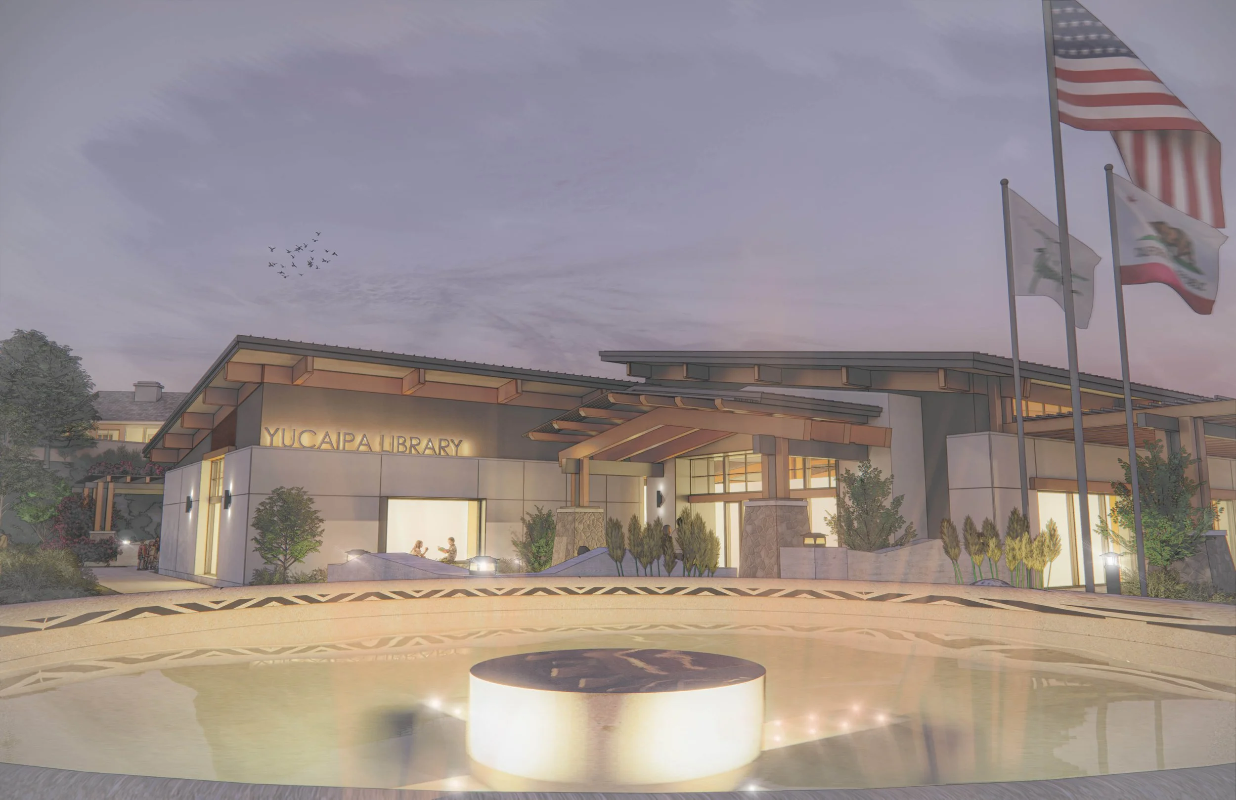 Exterior view of Yucaipa Library with flags flying in front and a fountain in the foreground during dusk.