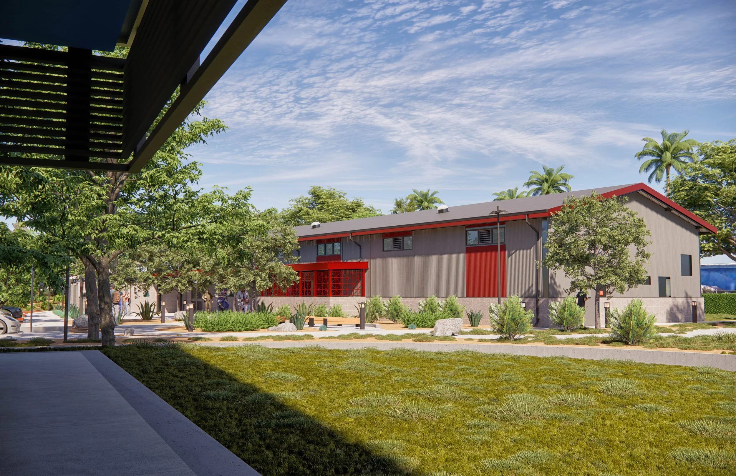 A modern building with gray and red exterior, surrounded by greenery and trees, under a blue sky with wispy clouds.