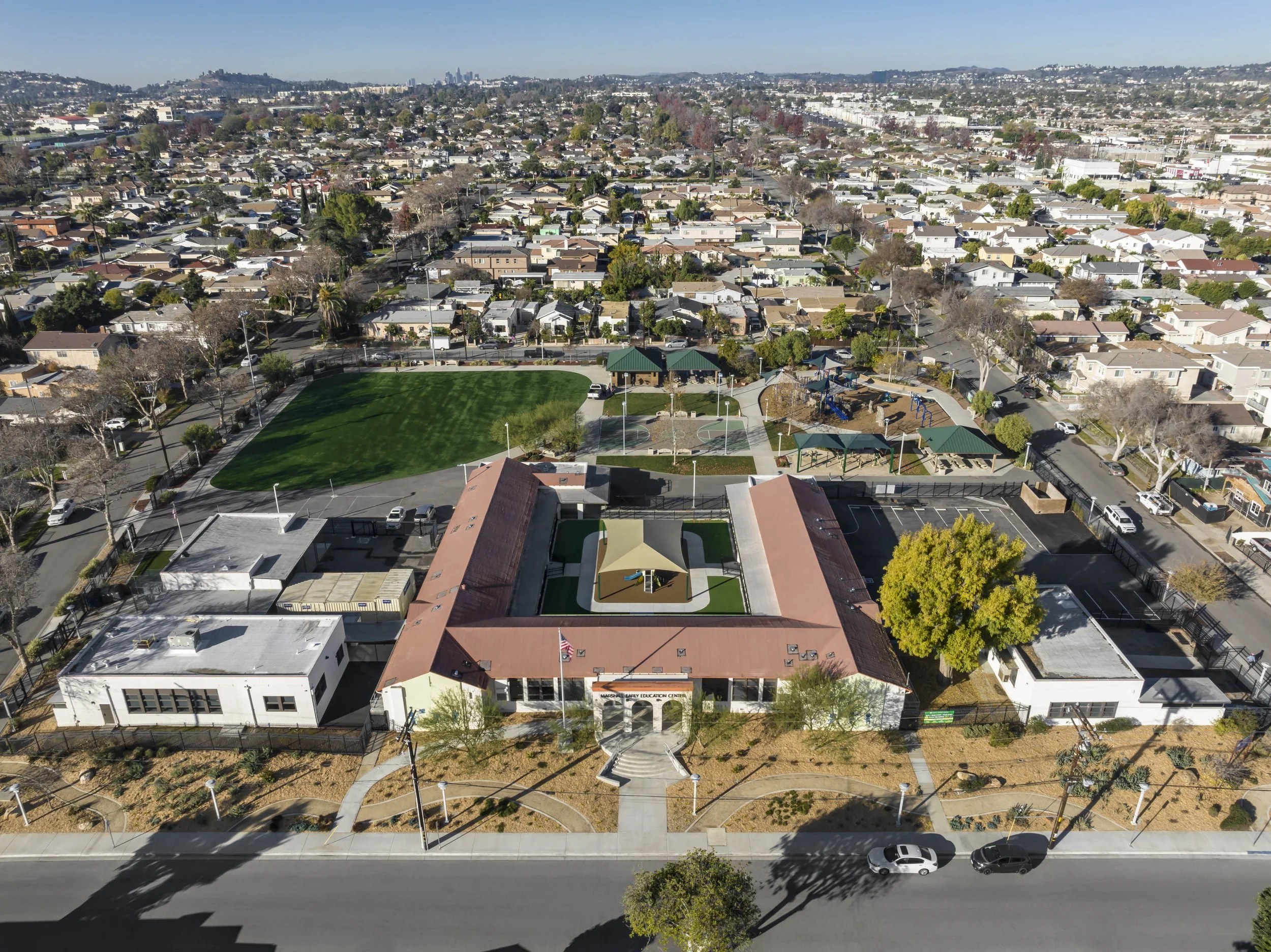 Aerial view of a school campus with buildings, a playground, a green field, and surrounding neighborhood houses in daytime.