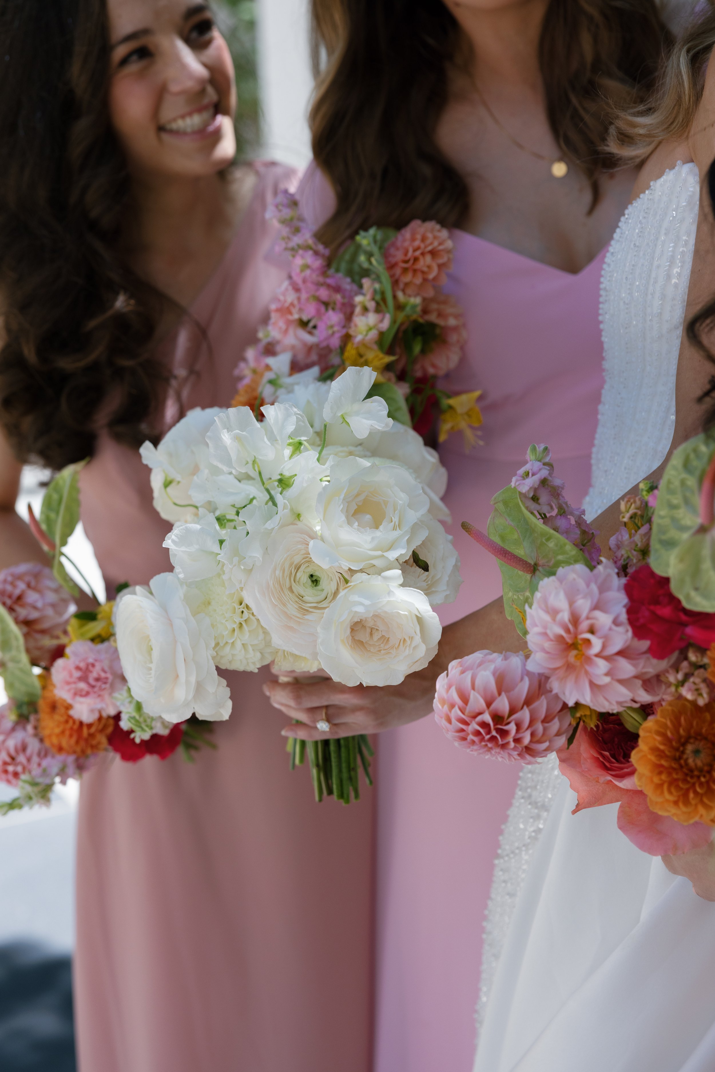 Close-up of a group of women holding floral bouquets, dressed in pink and white, attending a celebration or wedding event.