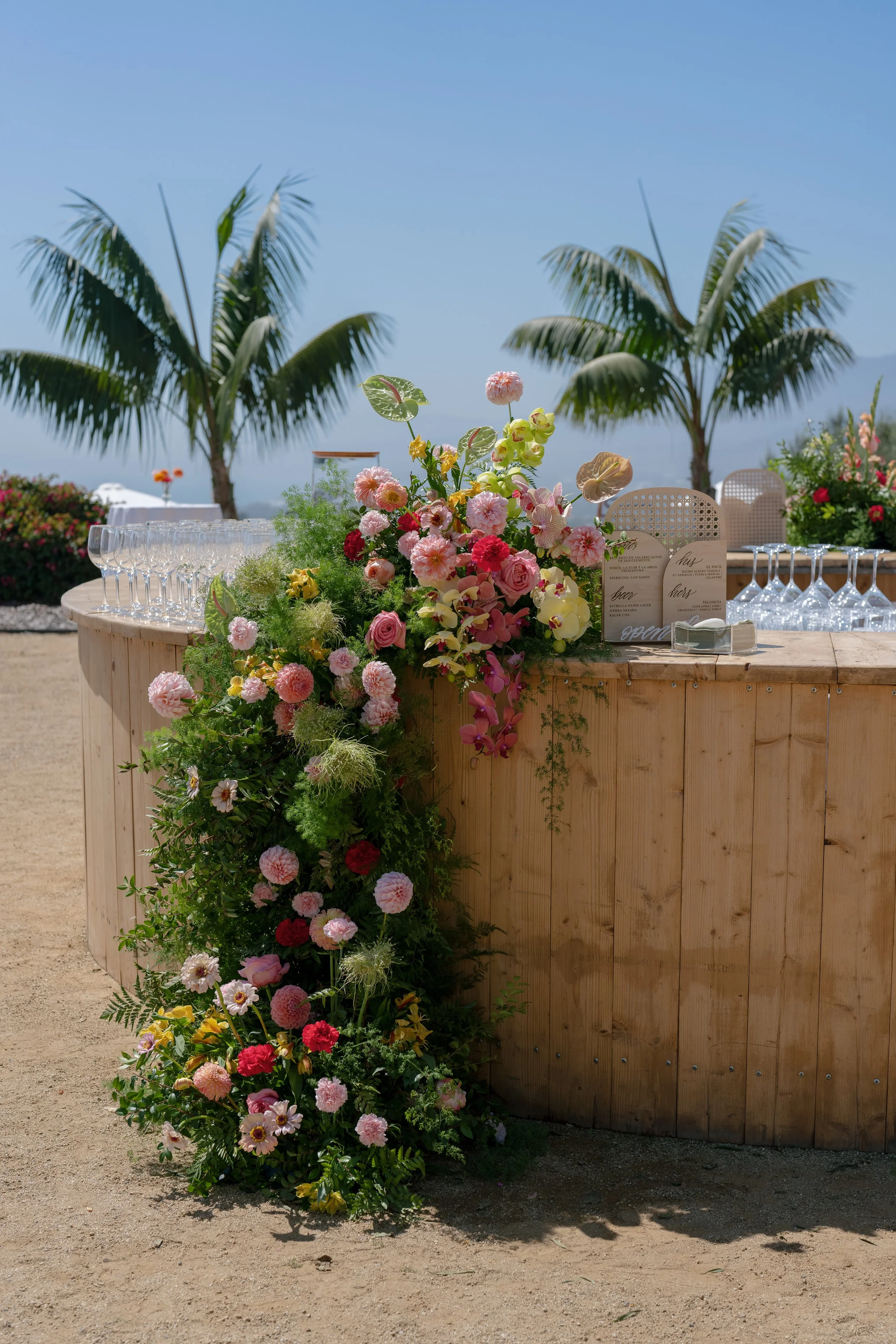 A floral arrangement on a wooden stand outdoors with palm trees and blue sky in the background.