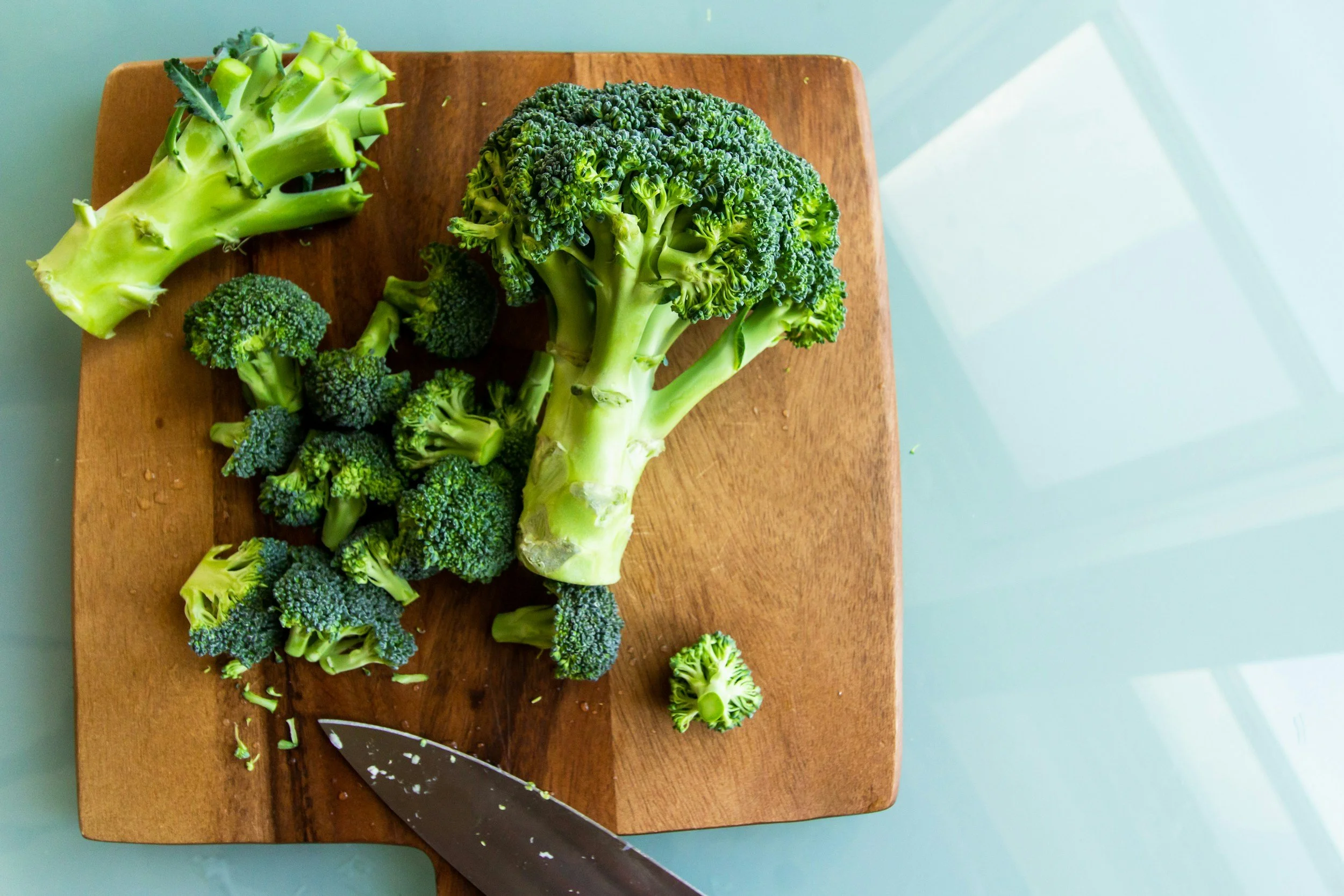 Fresh broccoli, chopped up on a cutting board.