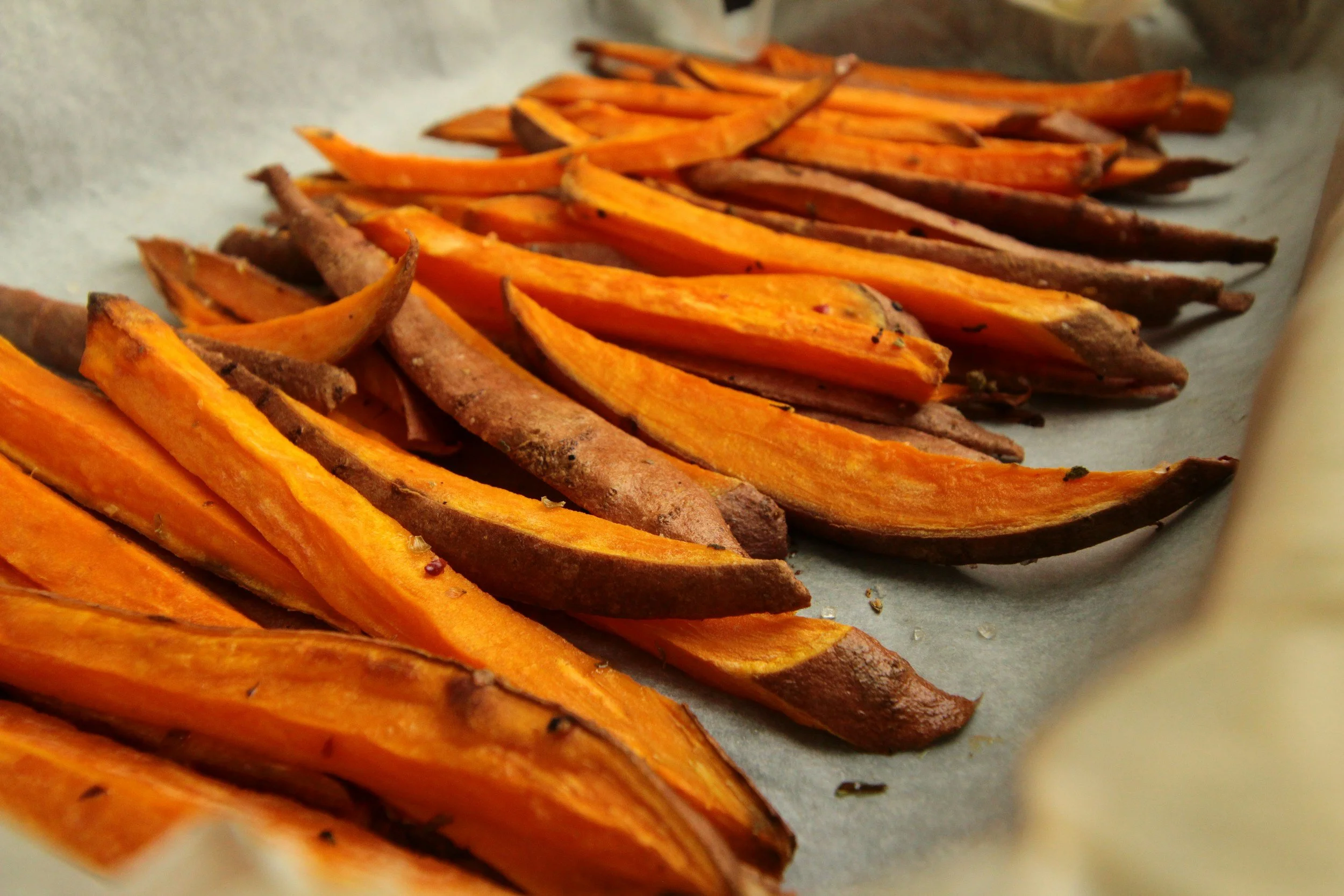 Baked sweet potato wedges spread out on parchment-lined baking tray.