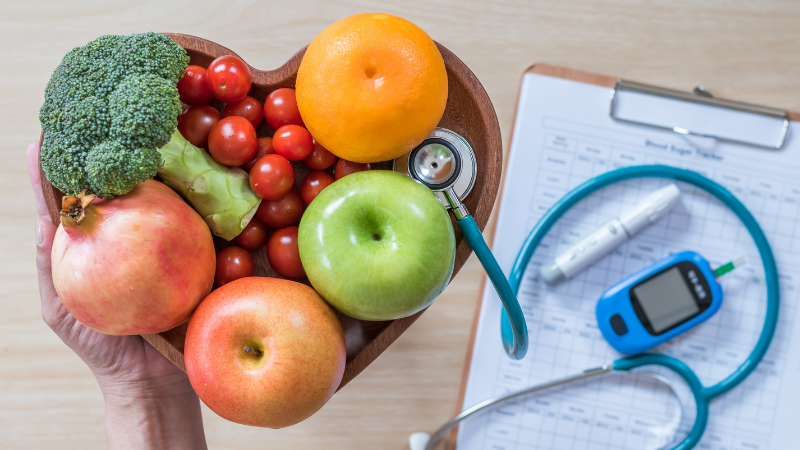Plated of fruits and vegatables next to a doctor's chart, stethascope, semiglutide injection, and blood sugar monitor.
