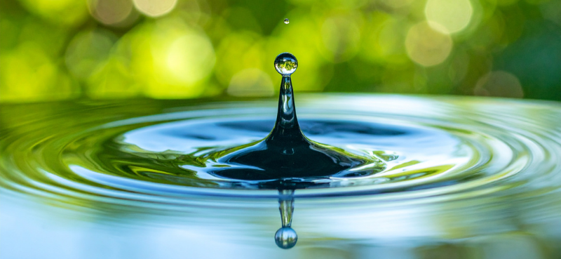 A water droplet in a pond with waves rippling outward, meant to represent the "ripple effect" of positive, health-promoting human behaviors.