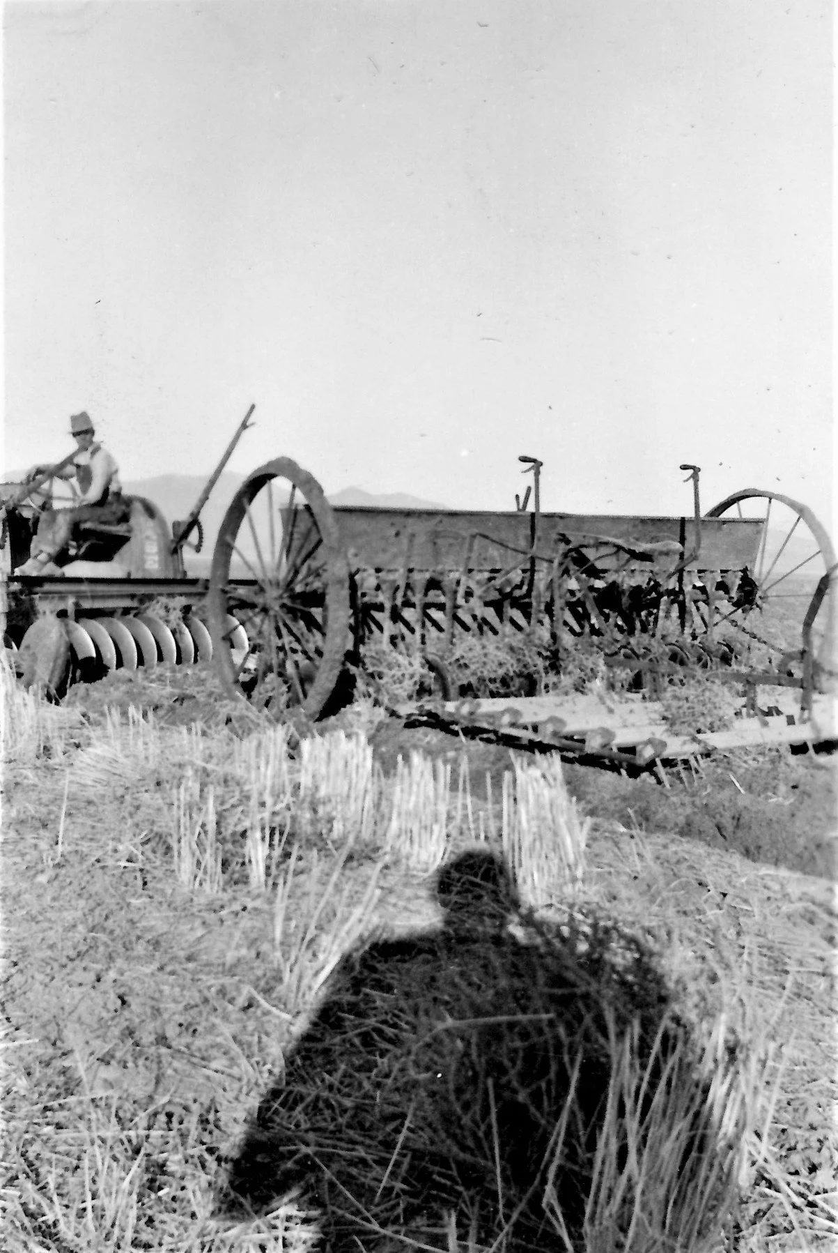 Henry Schmidt on a tractor in a field with agricultural equipment and harvested crops, with mountains in the distance.