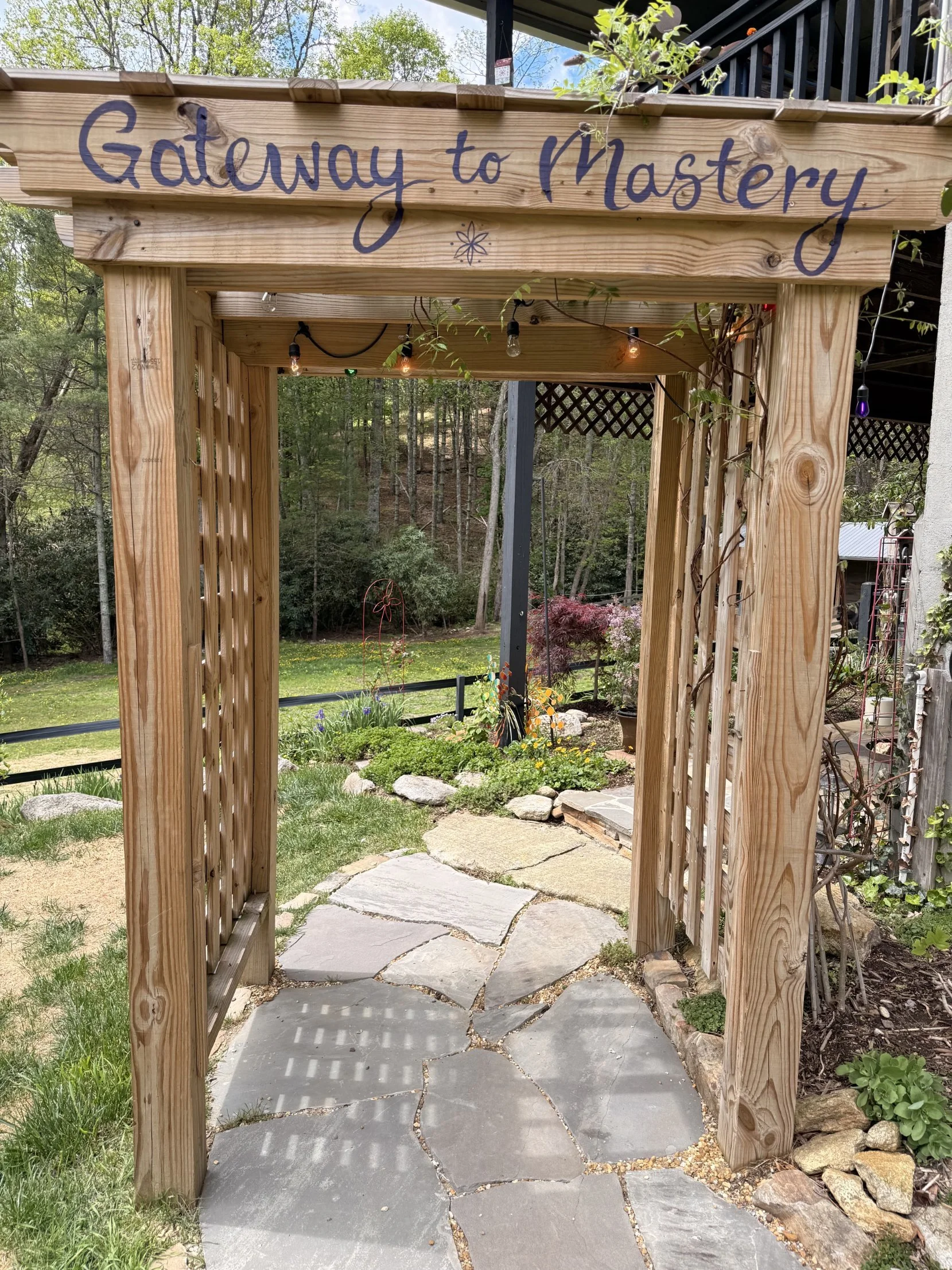 The hand-painted "Gateway to Mastery" arbor and stone path leading into the garden at Kyra's farm in Cullowhee