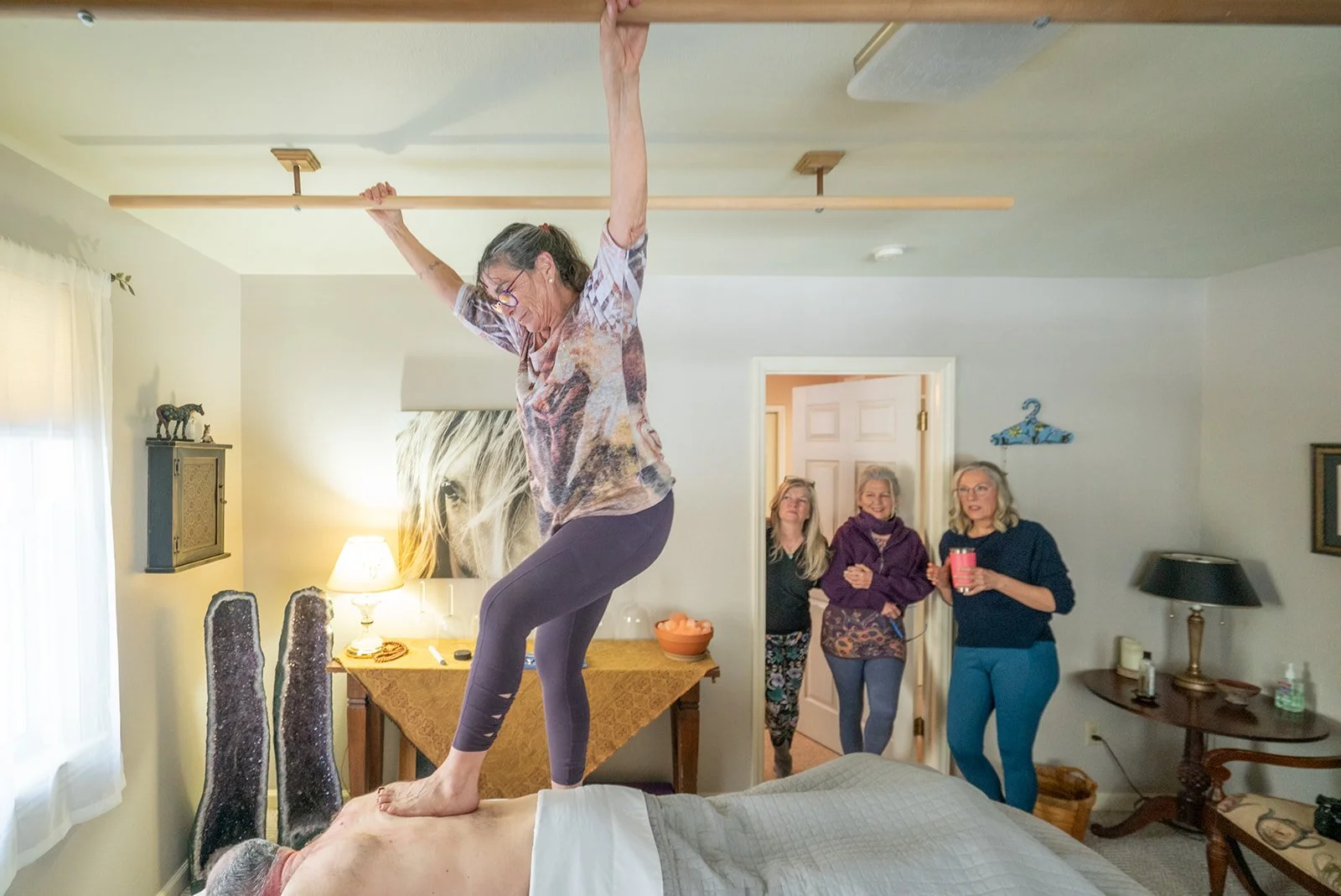 Kyra balancing on a client's back with her arms up during an Ashiatsu session while friends watch