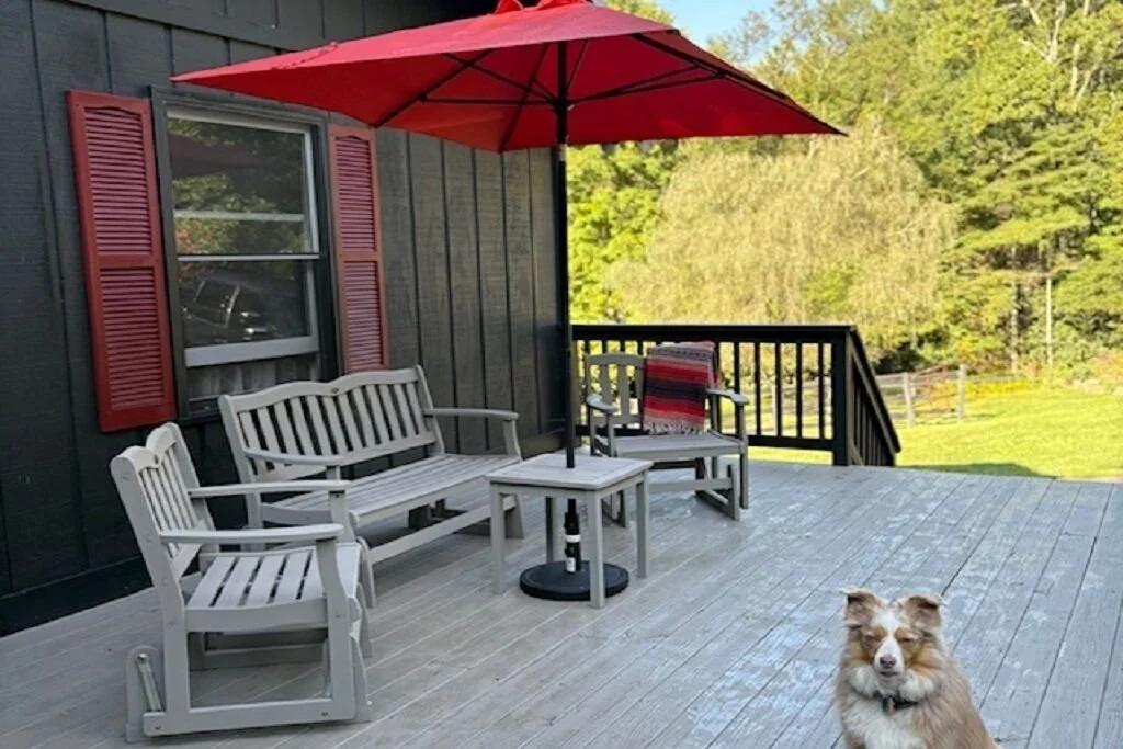 The farm house deck with benches under a red umbrella, with a dog lounging nearby