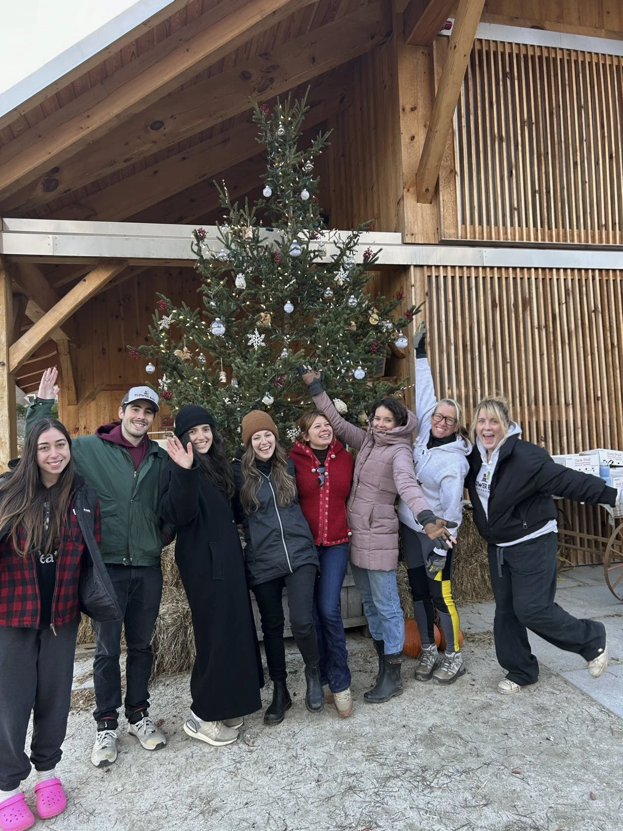 Group of people posing in front of a decorated Christmas tree outside a wooden cabin.