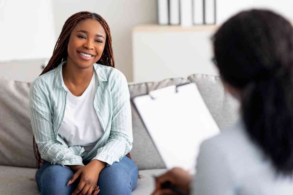 Woman smiling during a conversation with a therapist holding a clipboard.
