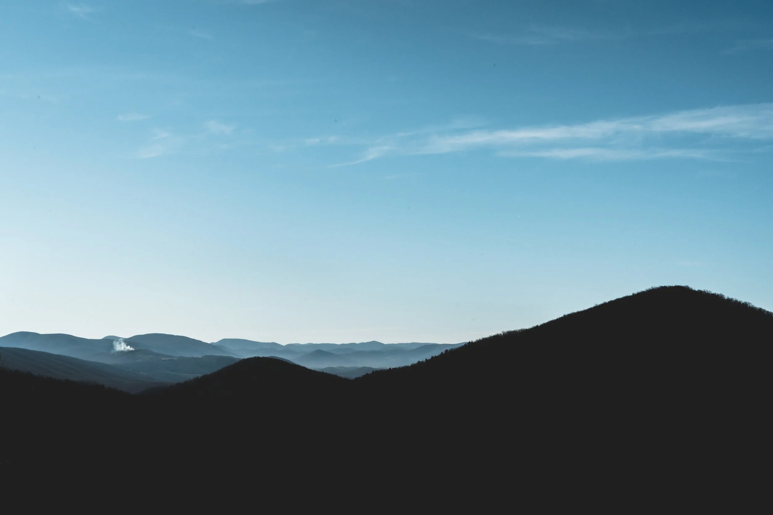 Silhouetted mountain range against a blue sky with wispy clouds.