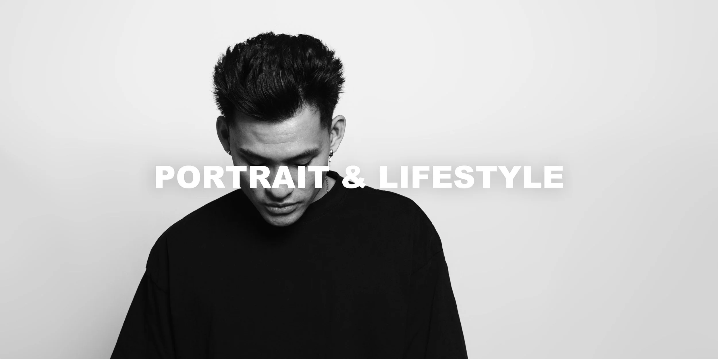 Black and white photo of a young man with styled hair, wearing a black top, looking down