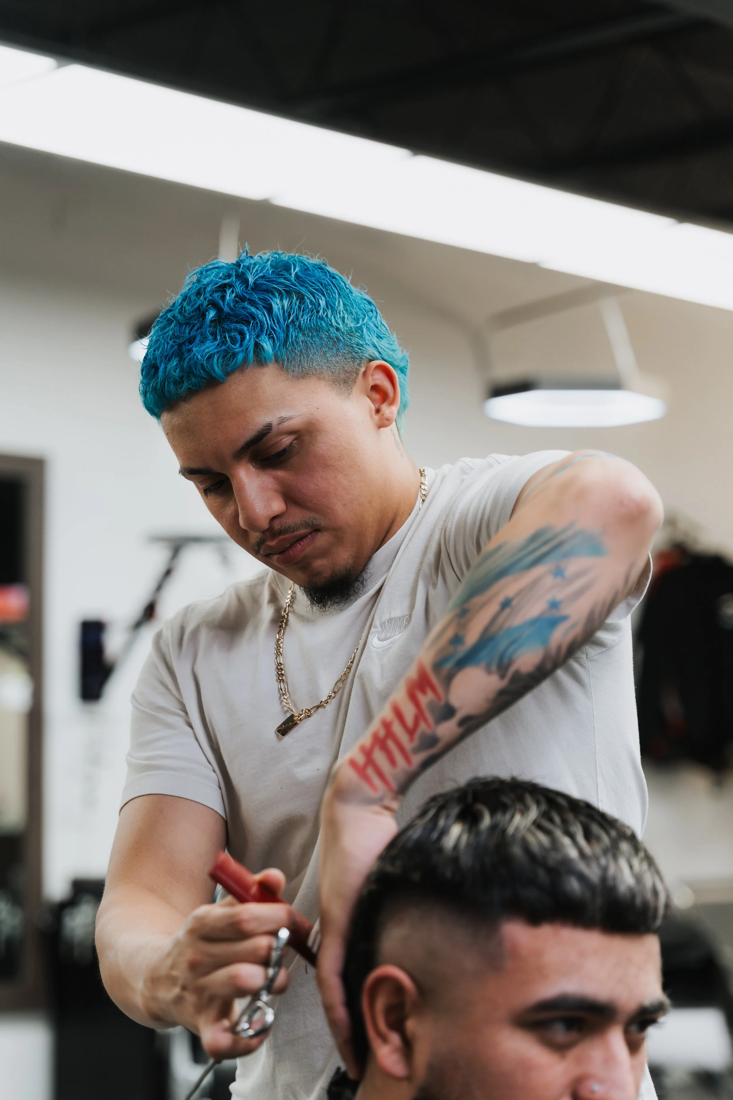Barber with blue hair trimming a customer's hair in a salon.
