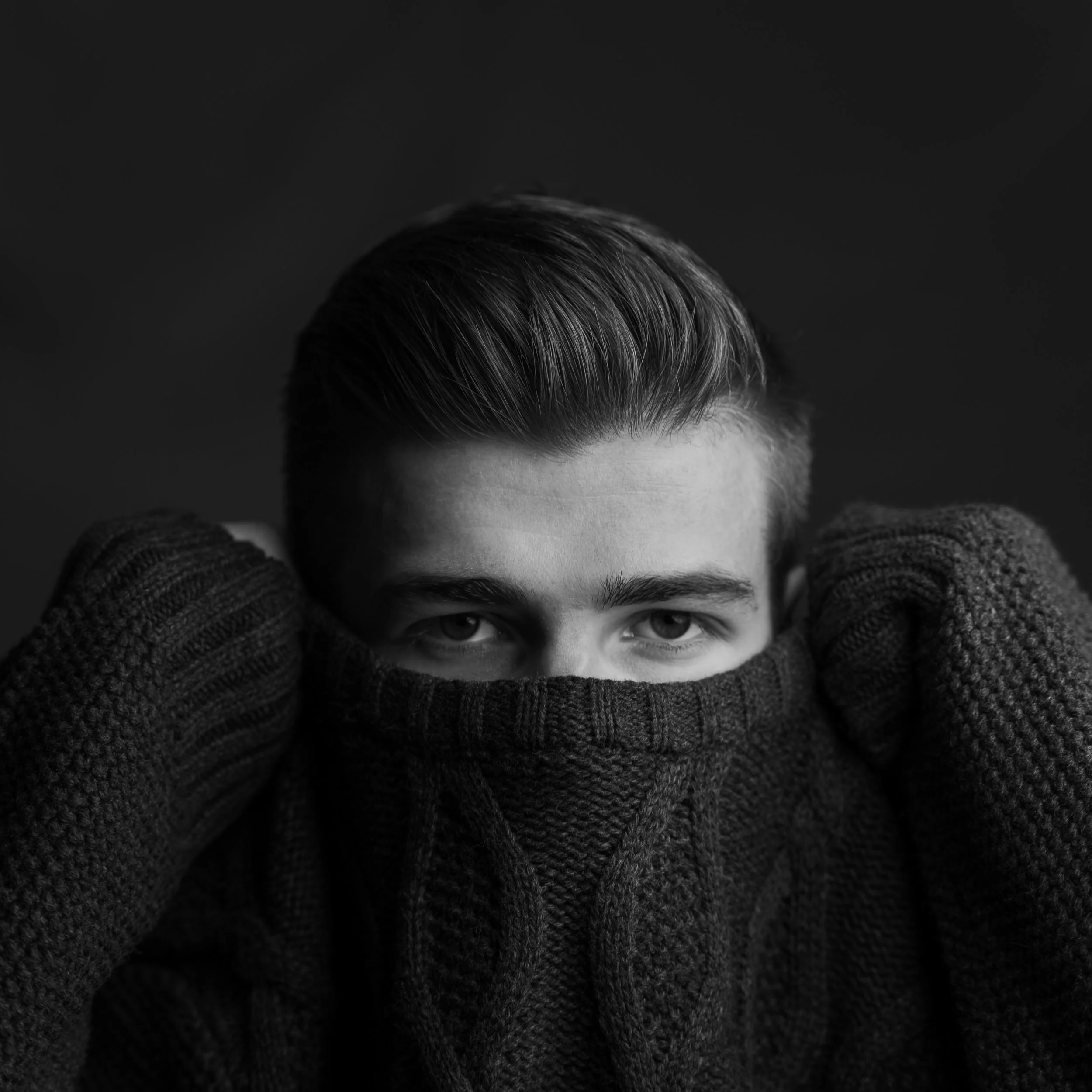 Black and white portrait of a young man with styled hair, partially concealed by a high-collared sweater.