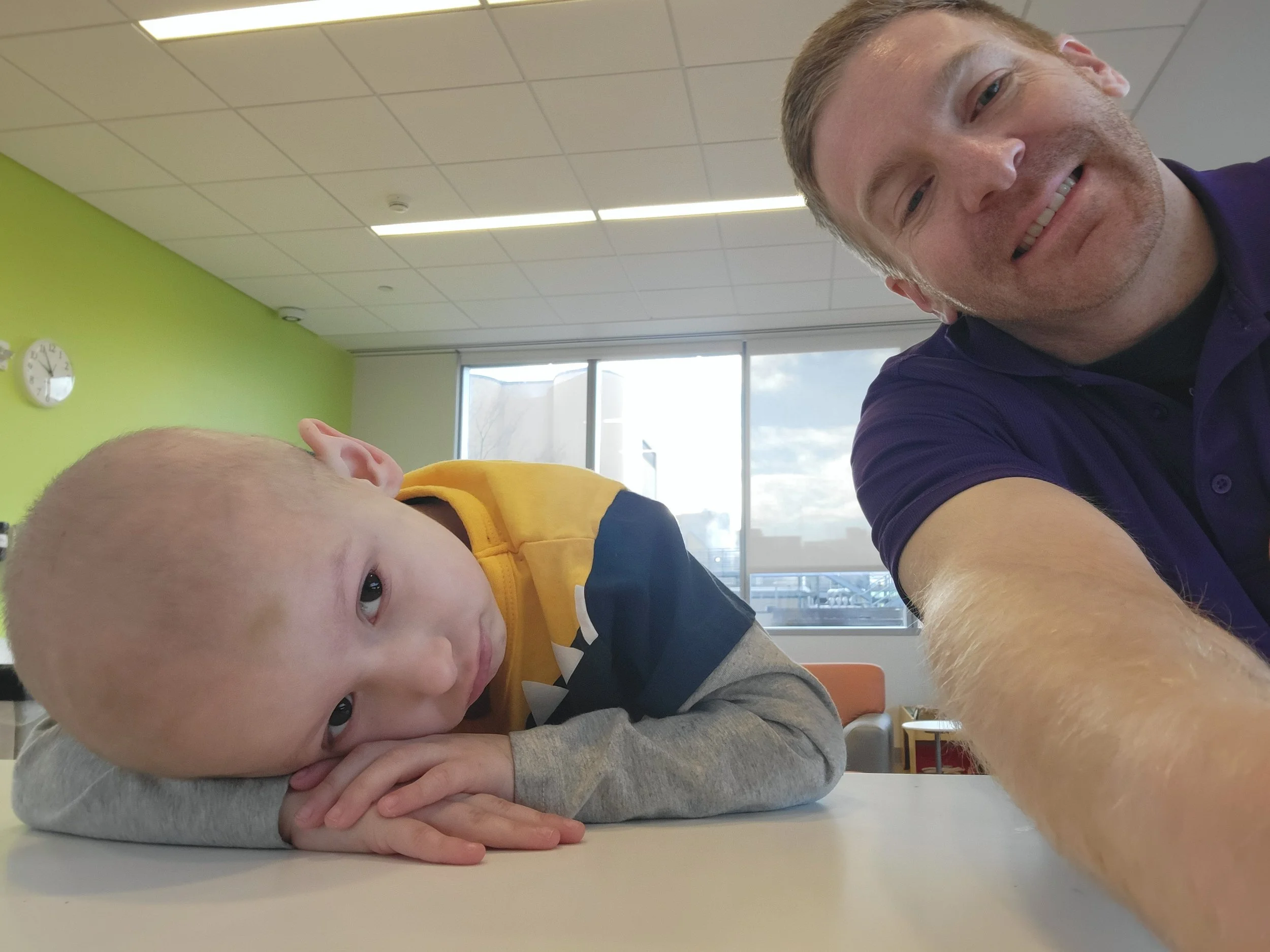 Male JoyRx Mentor in purple polo taking a selfie with mentee, a young boy who is bald and being coy for the camera.