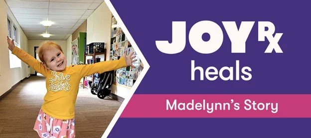 Young girl smiles with her arms held out in a pose of victory.