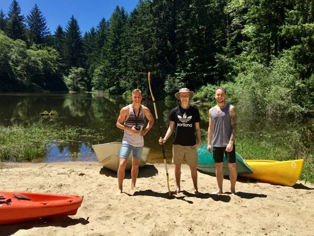 Three young men stand in front of three kayaks.