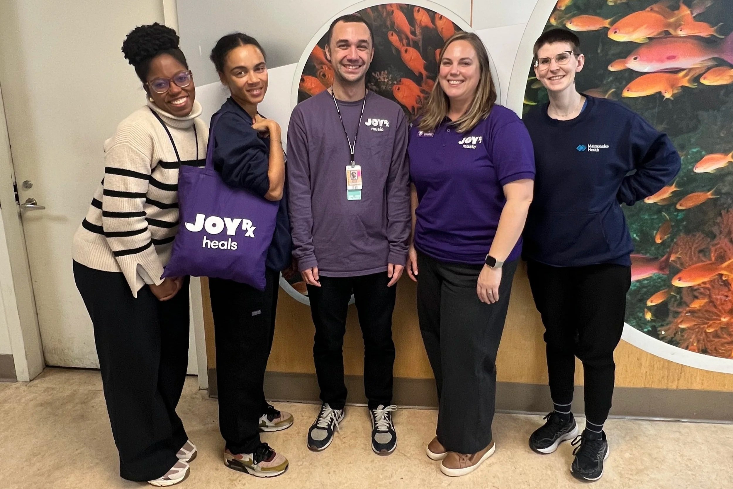 A group of five adults wearing purple stand in front of a wall with fish pictures in a hospital.