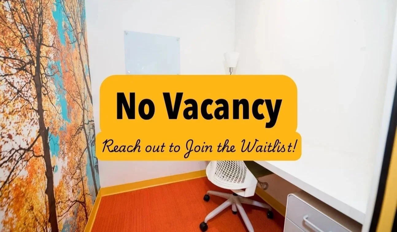 Workspace with a white desk, an ergonomic white chair, a lamp, a cork board, and an autumn tree pattern on the left wall, with orange carpet and yellow baseboards.