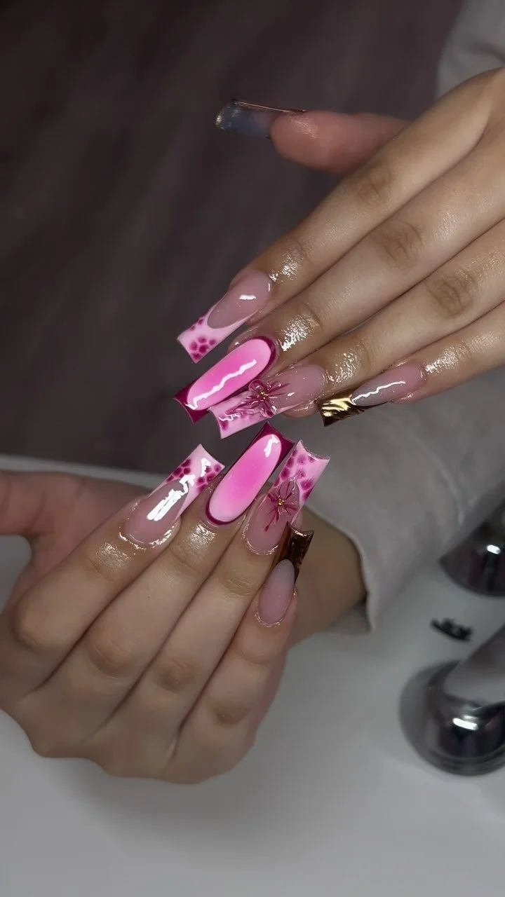 Close-up of a person's hands showcasing long, decorated pink acrylic nails with floral and abstract designs.