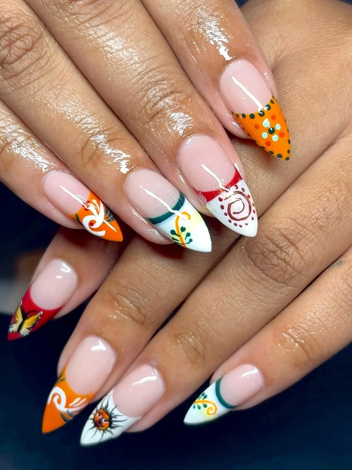Colorful, decorative nail art with orange, red, green, black, and white patterns on almond-shaped nails.