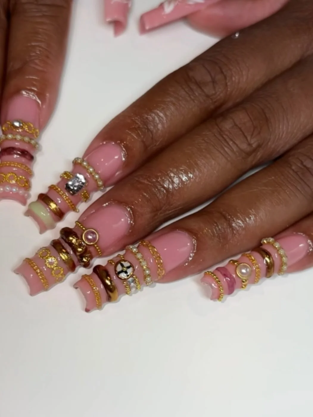 Close-up of a hand with long, manicured nails on a white surface, adorned with multiple gold and jeweled rings.
