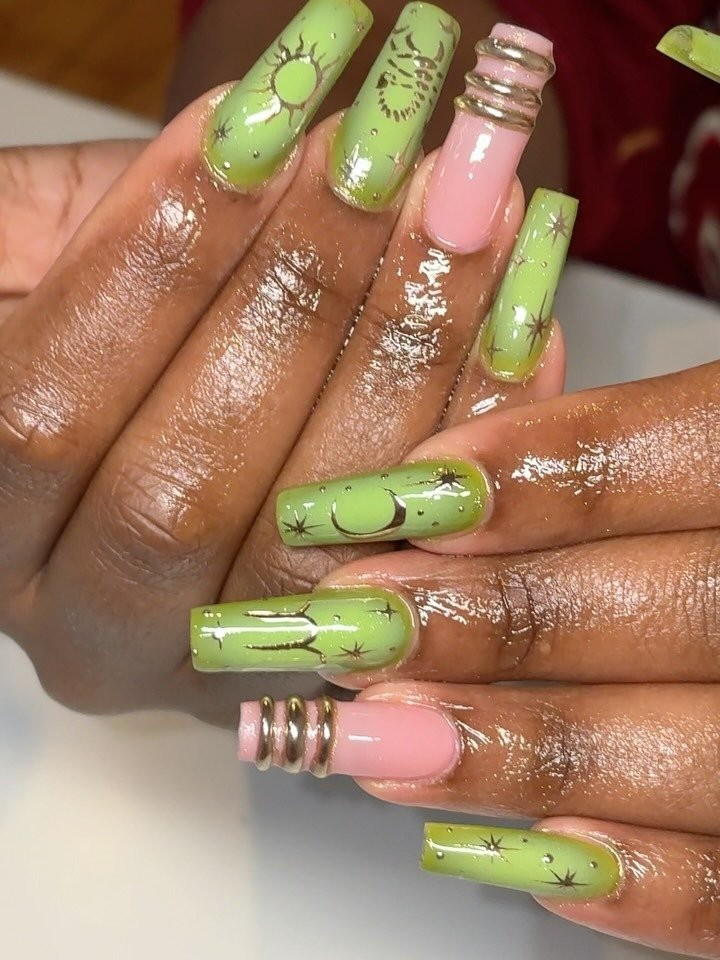 Close-up of manicured nails with green and pink polish, decorated with celestial designs like moons, stars, and suns, with some nails wrapped in silver coils.