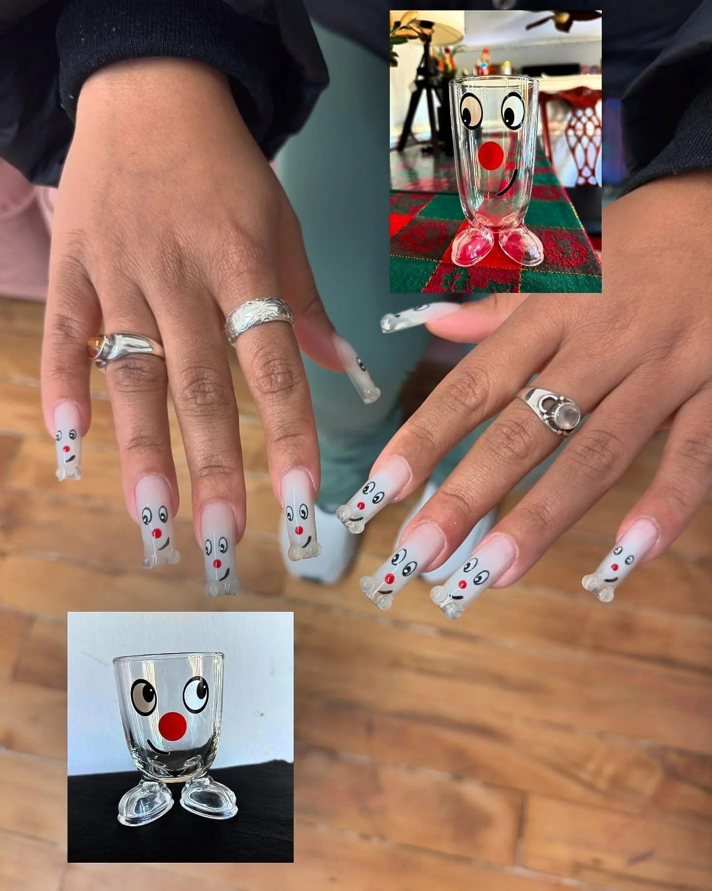 Person showing off Christmas-themed nail art resembling snowmen, with glasses featuring eyes, a red nose, and a smiling mouth, in front of a wooden floor. Two decorated glasses with face designs, one on a table with a red and green cloth and another 
