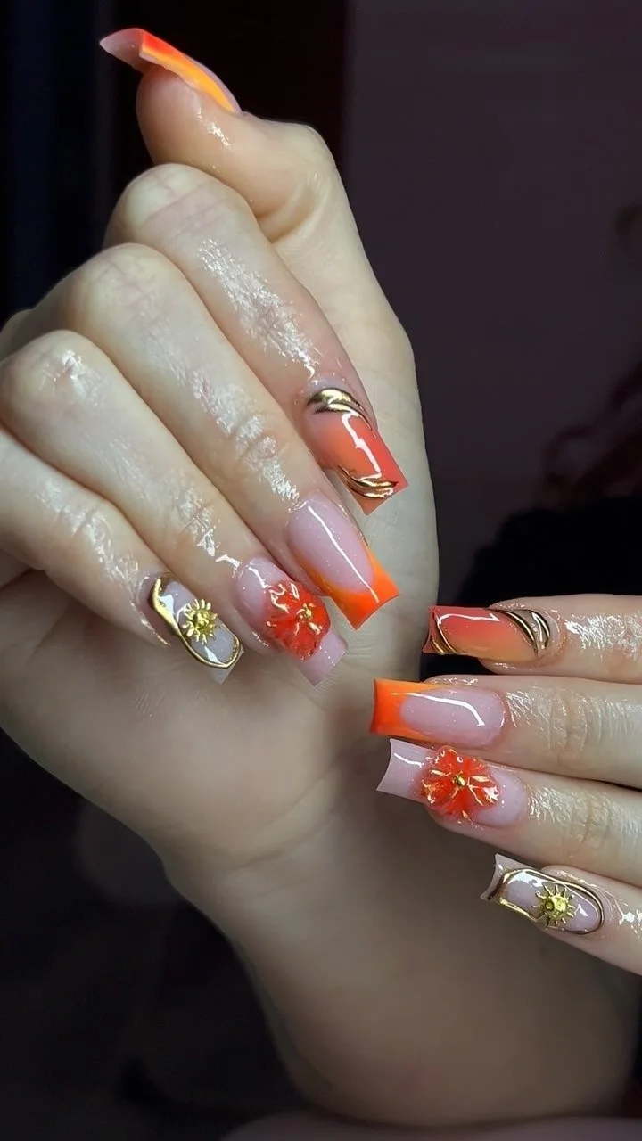 Close-up of manicured fingernails featuring orange and nude acrylic nails with floral and gold accents.