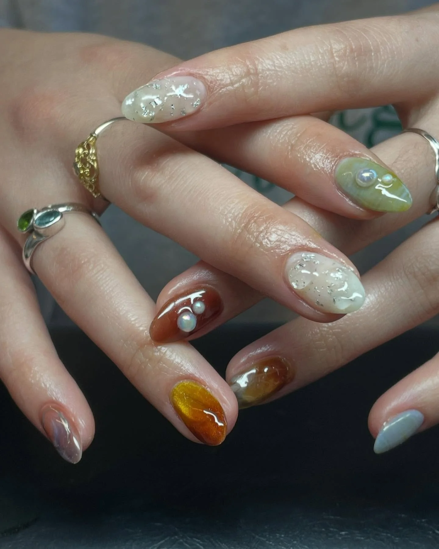 Close-up of hands with intricate multi-color nail art and multiple rings.