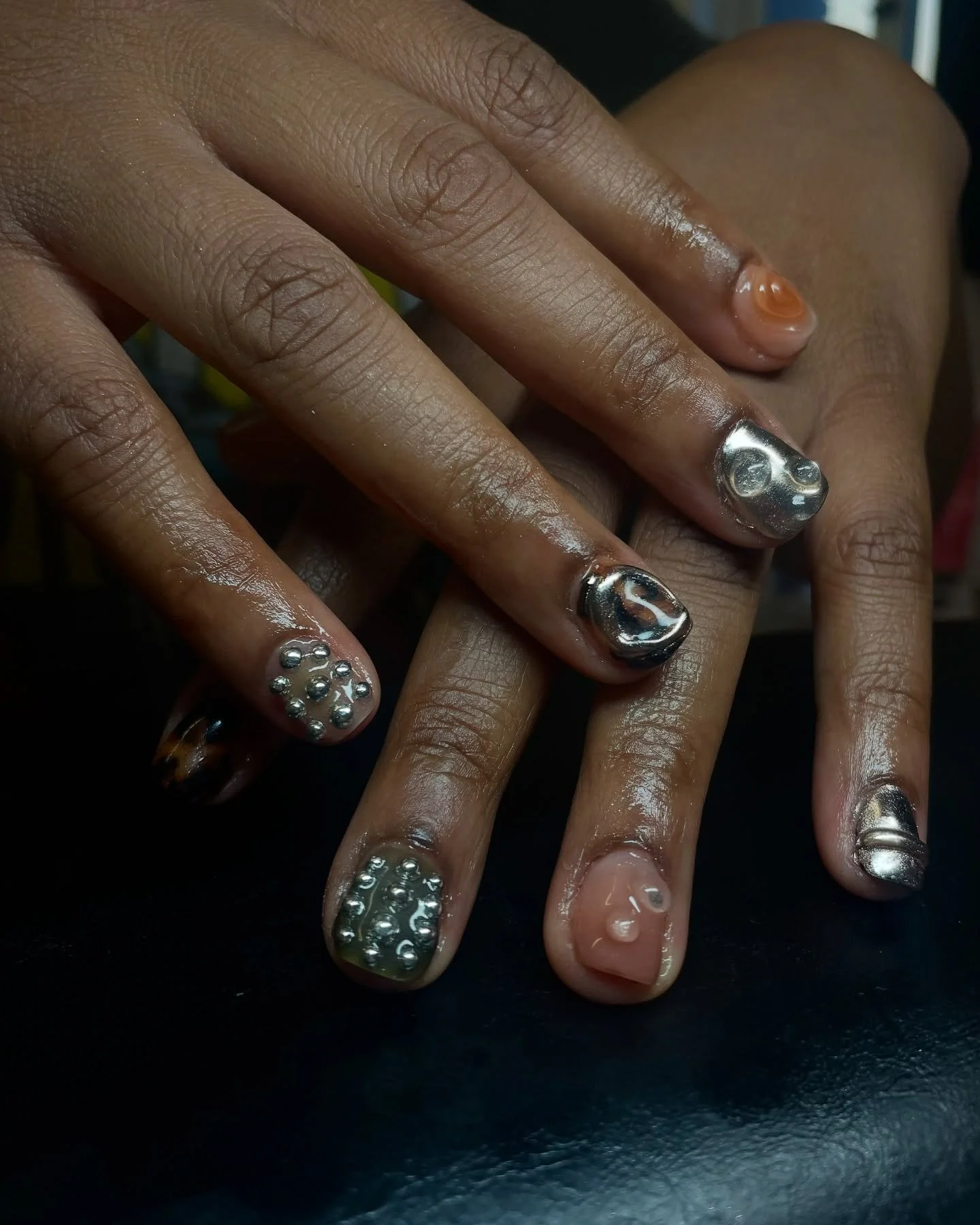 Close-up of hands with metallic nail art, some nails decorated with silver studs and others with metallic and abstract designs.