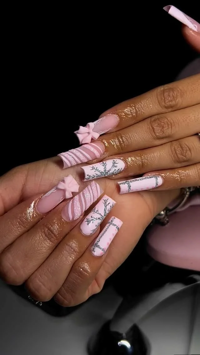 Close-up of hands with elaborate pink and white Christmas-themed nail art, including bows, stripes, and glittery branches.