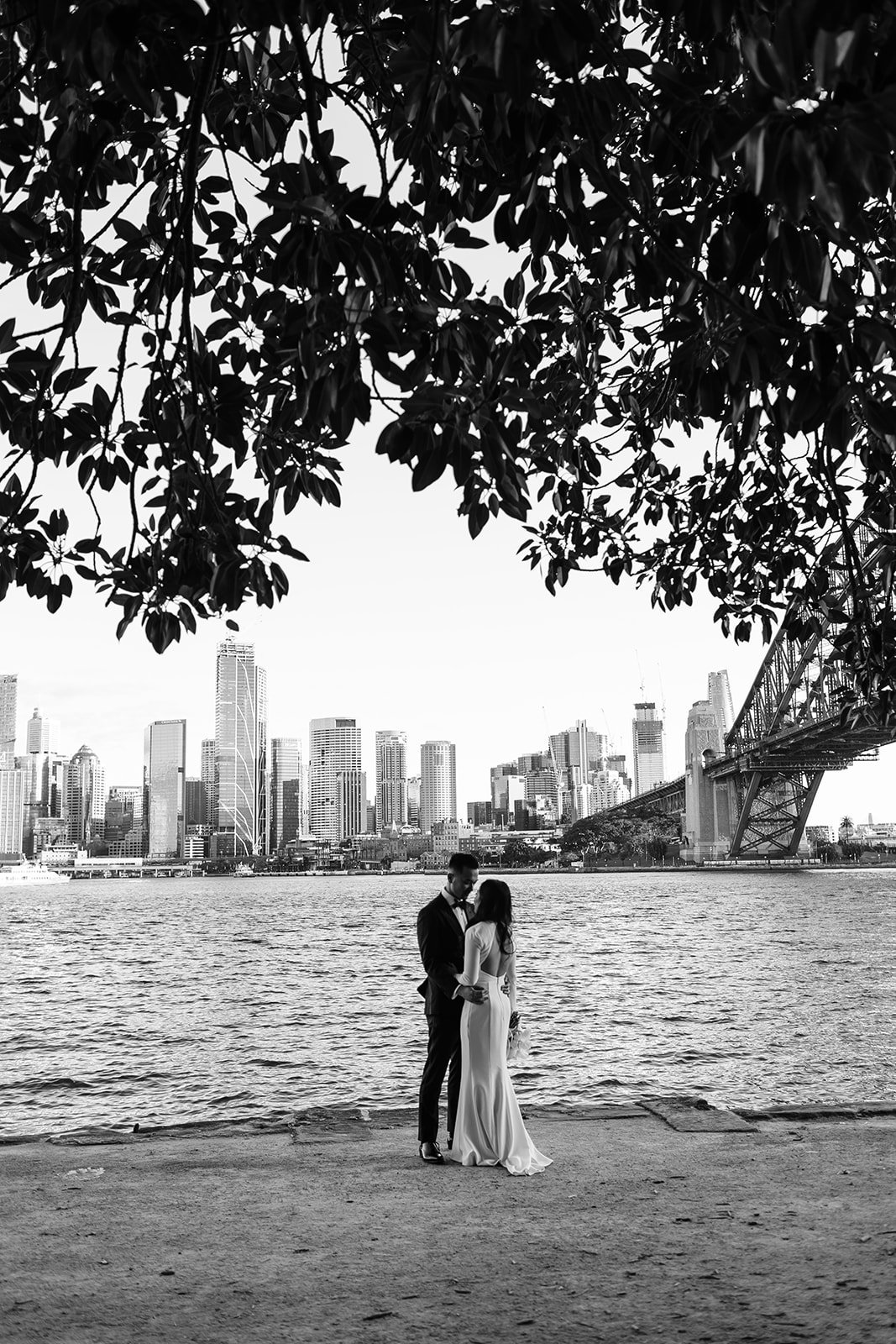 Black and white photo of bride and groom at Kirribili Lookout with the Sydney Harbour Bridge and Sydney skyline in the background