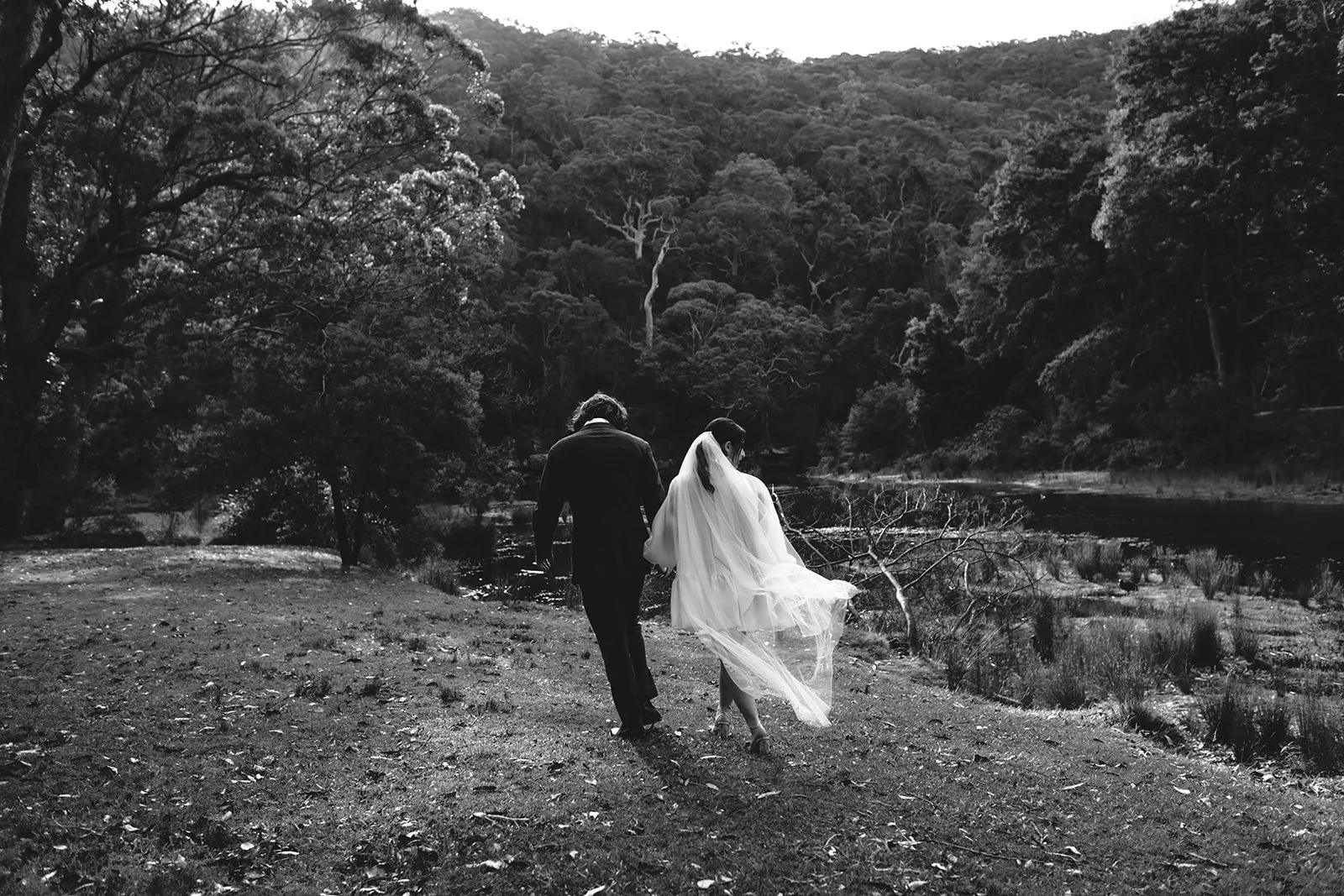 A black and white photo of a bride and groom walking hand in hand in the Royal National Park Sydney.