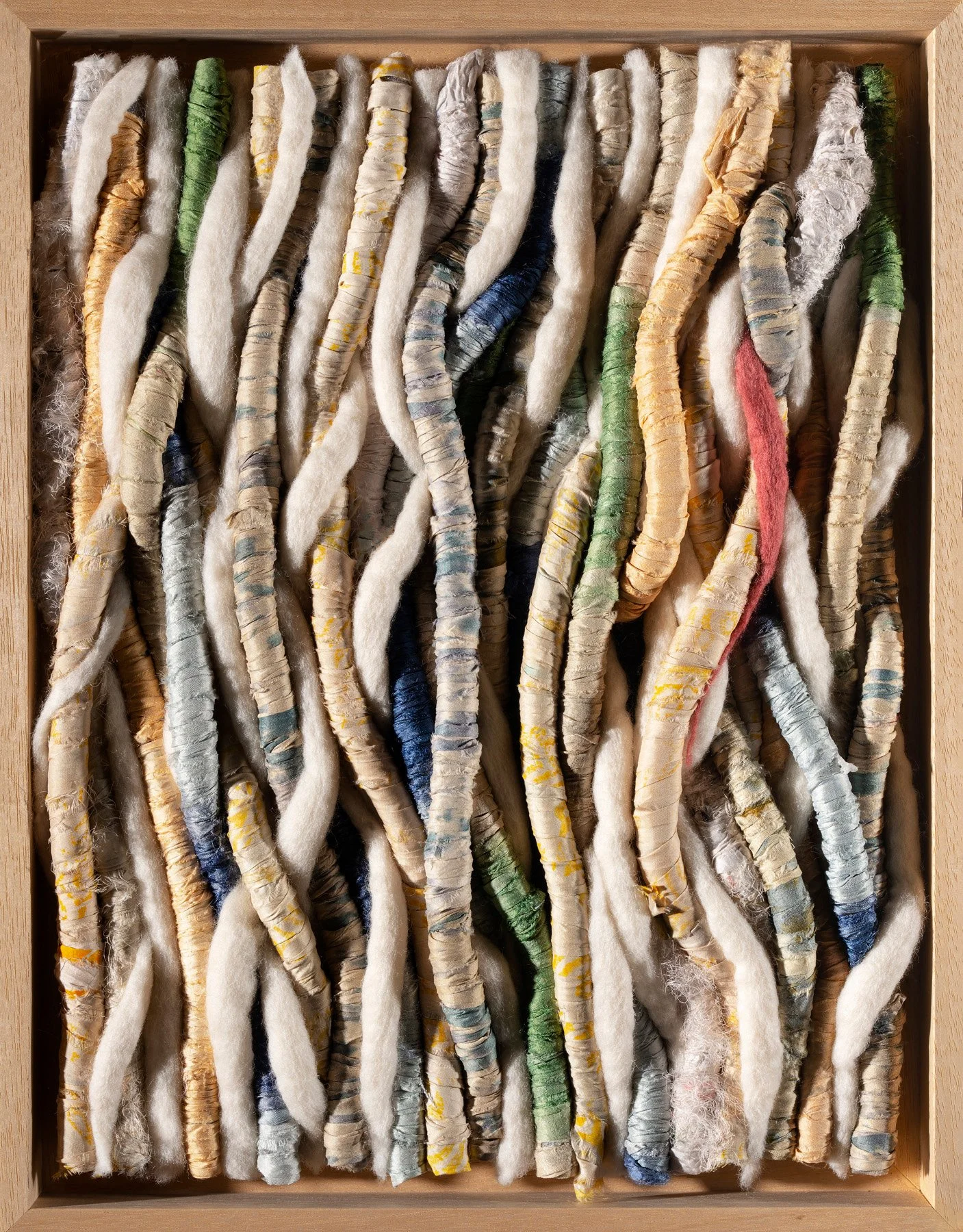 A collection of hand-rolled, colorful textile strips in a wooden box.