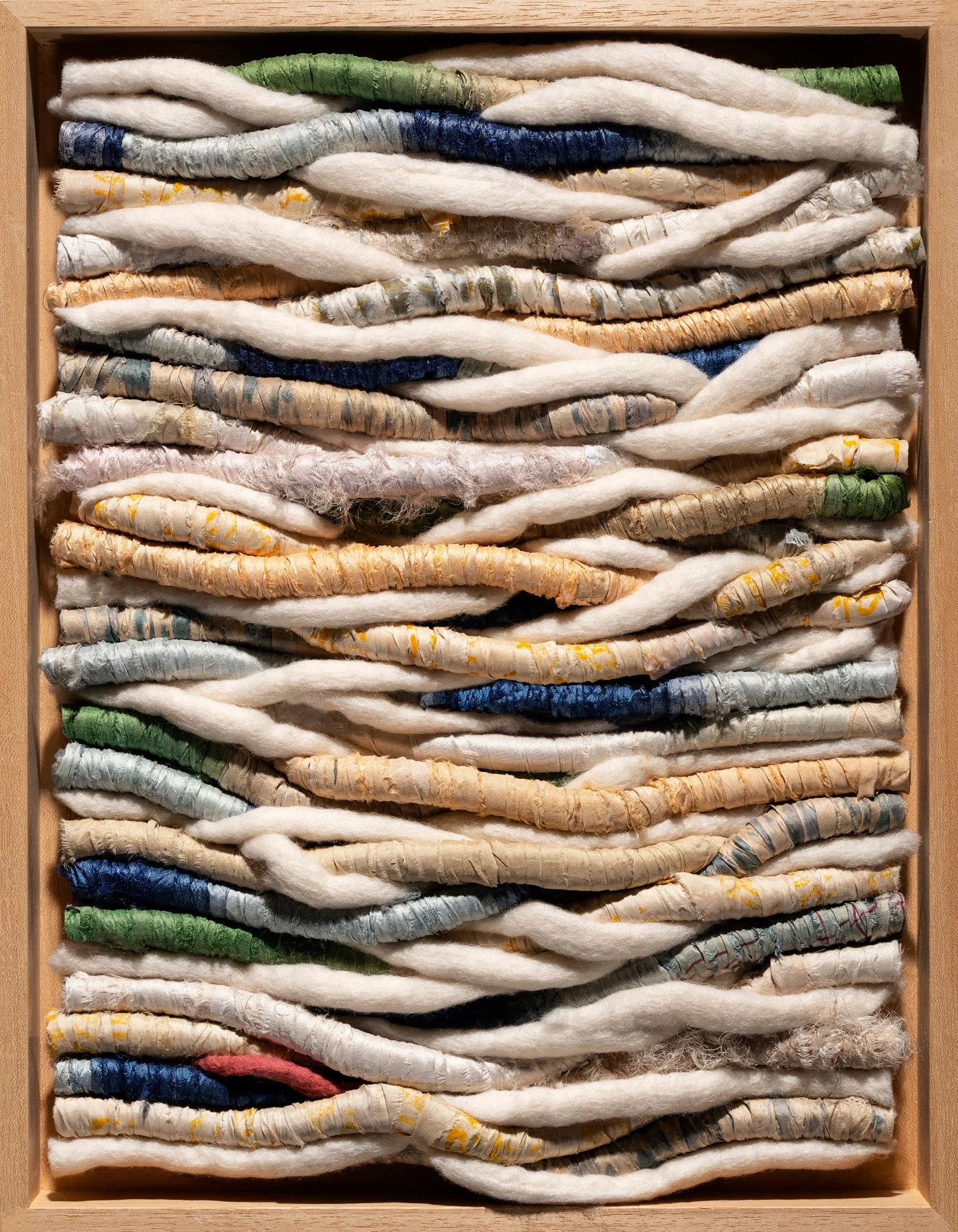 A framed installation of twisted and coiled fabric strips arranged in rows, with various colors and textures.