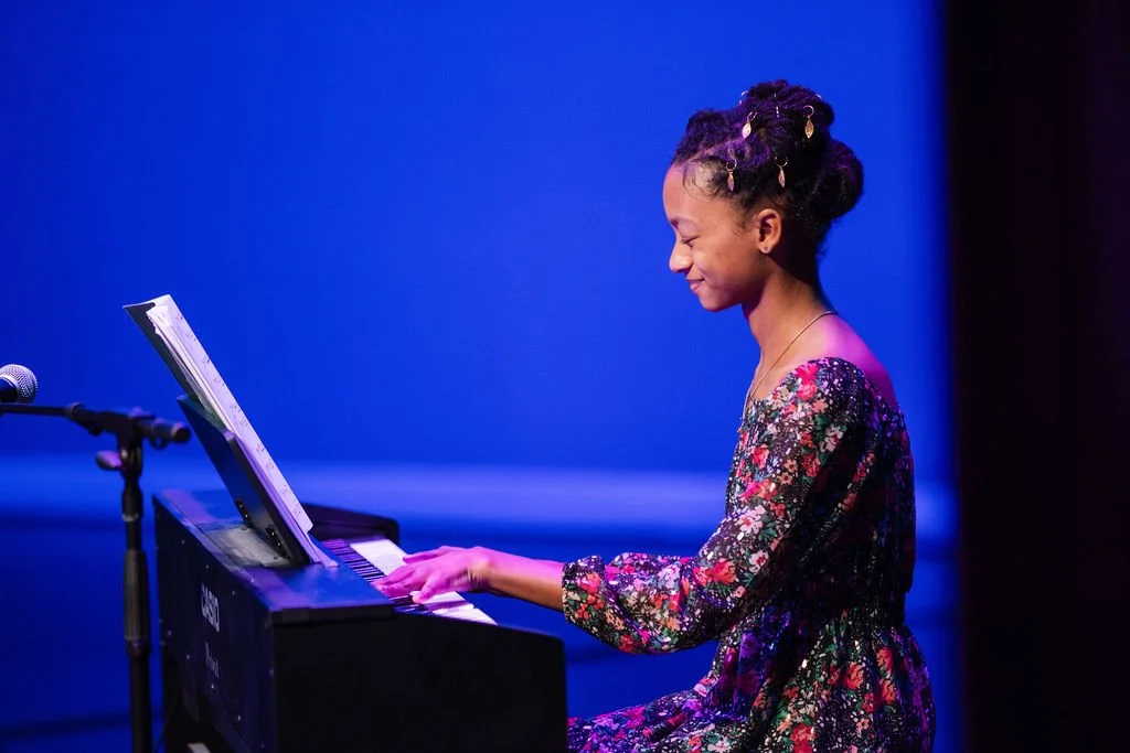 A young girl smiles while playing piano at a Learn Music recital in downtown Cornelius, NC
