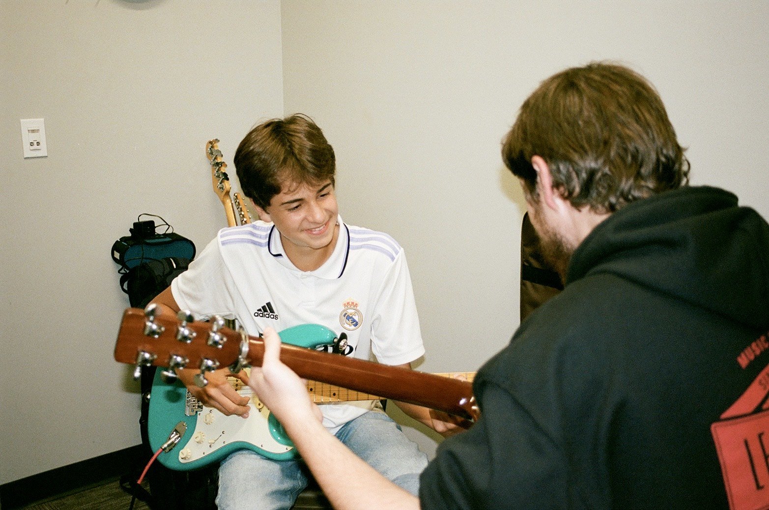 A young male student at Learn Music in Cornelius, NC smiles while playing guitar with his instructor