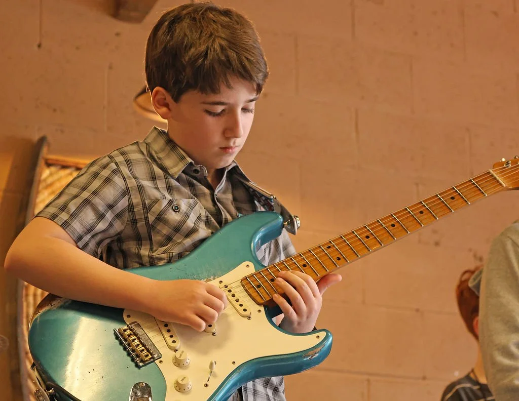 Young boy playing guitar at a student rock band concert