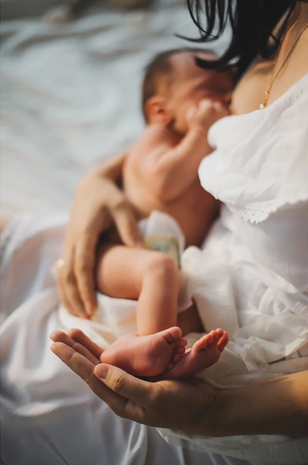 A parent holding a newborn close, with the baby's feet resting in their hand.
