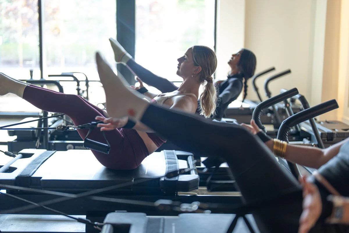 Women exercising on reformer Pilates machines in a fitness studio.