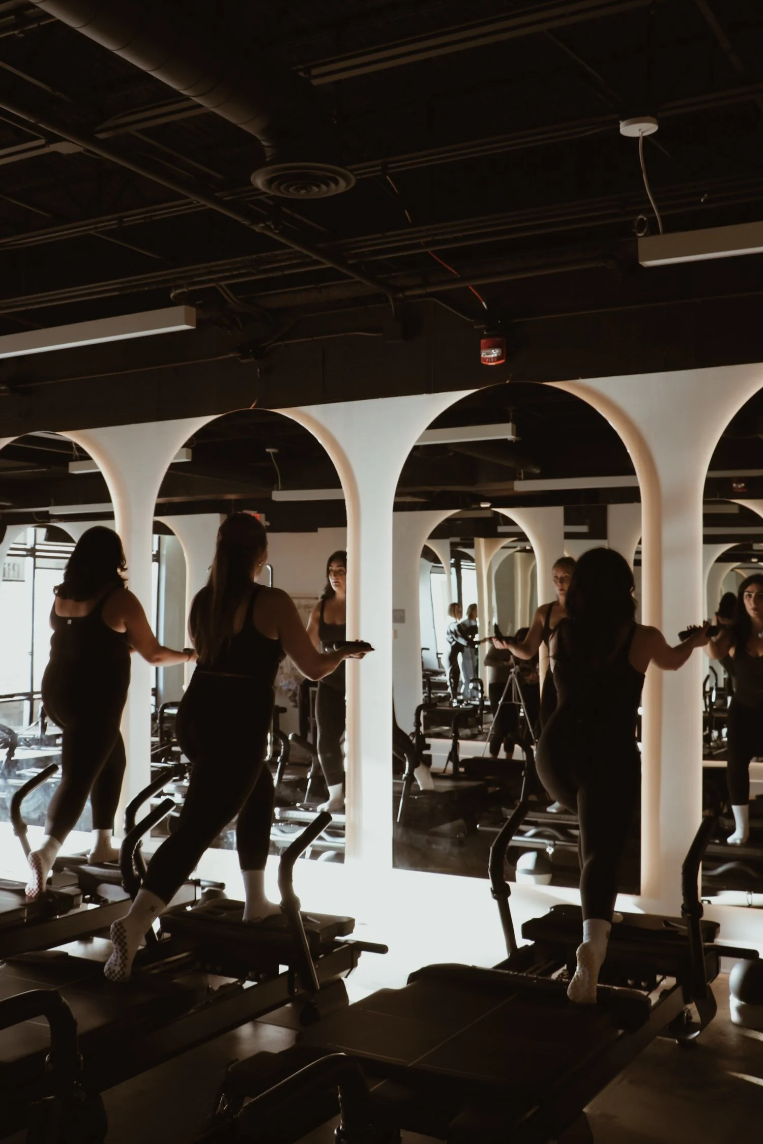 Women exercising on treadmills in a gym with modern, illuminated arches and black ceiling.
