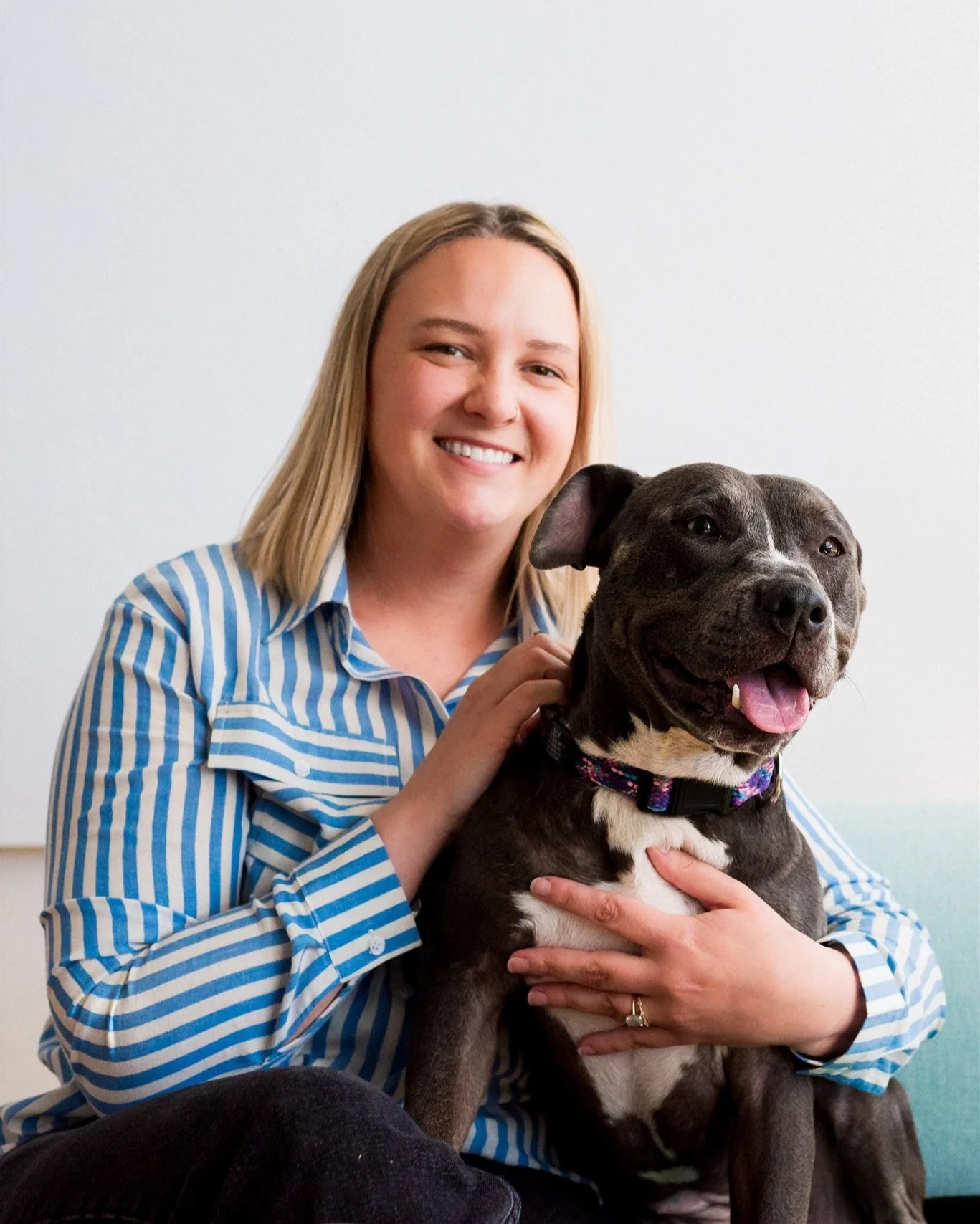 Woman smiling with a grey and white dog, wearing a striped shirt, sitting on a couch.